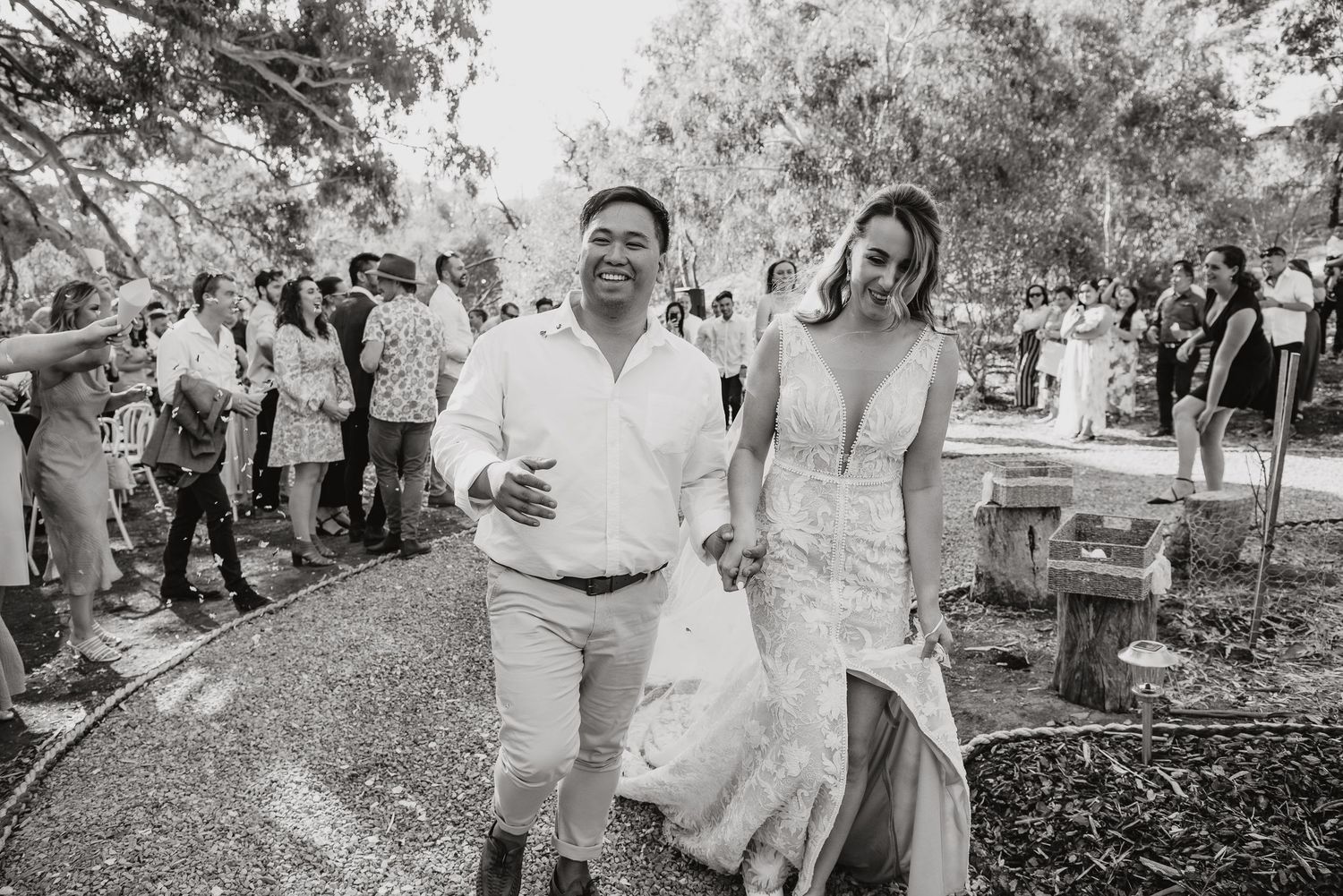 A joyful couple walks together at an outdoor celebration surrounded by guests in a black and white photo.