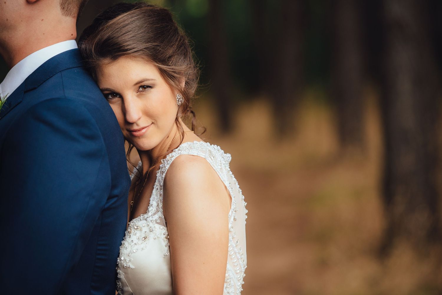 A close-up wedding portrait showing lace dress details in a forest setting with soft natural lighting.