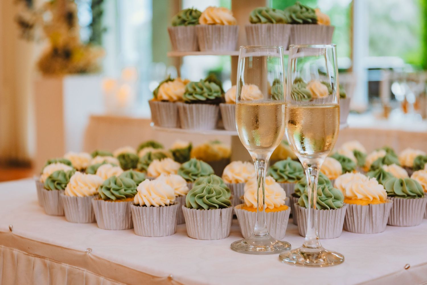 Elegant display of champagne flutes and cupcakes with green frosting at a wedding reception dessert table.