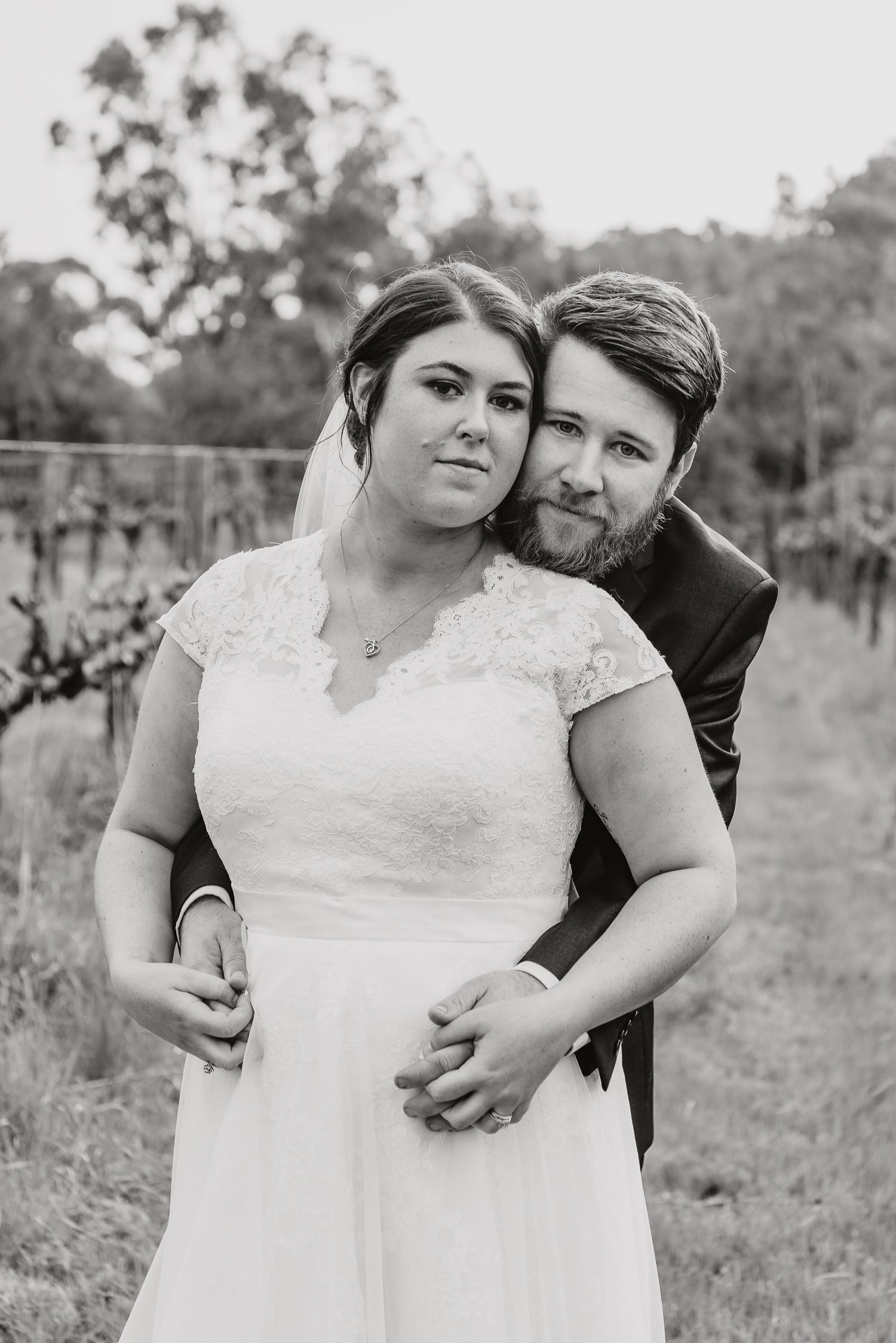 Black and white portrait of a bride and groom embracing in an outdoor vineyard setting.