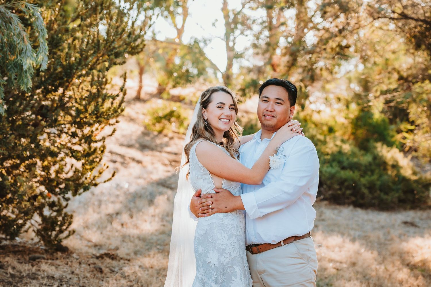 Newlywed couple embraces during golden hour wedding photoshoot in a scenic outdoor setting.