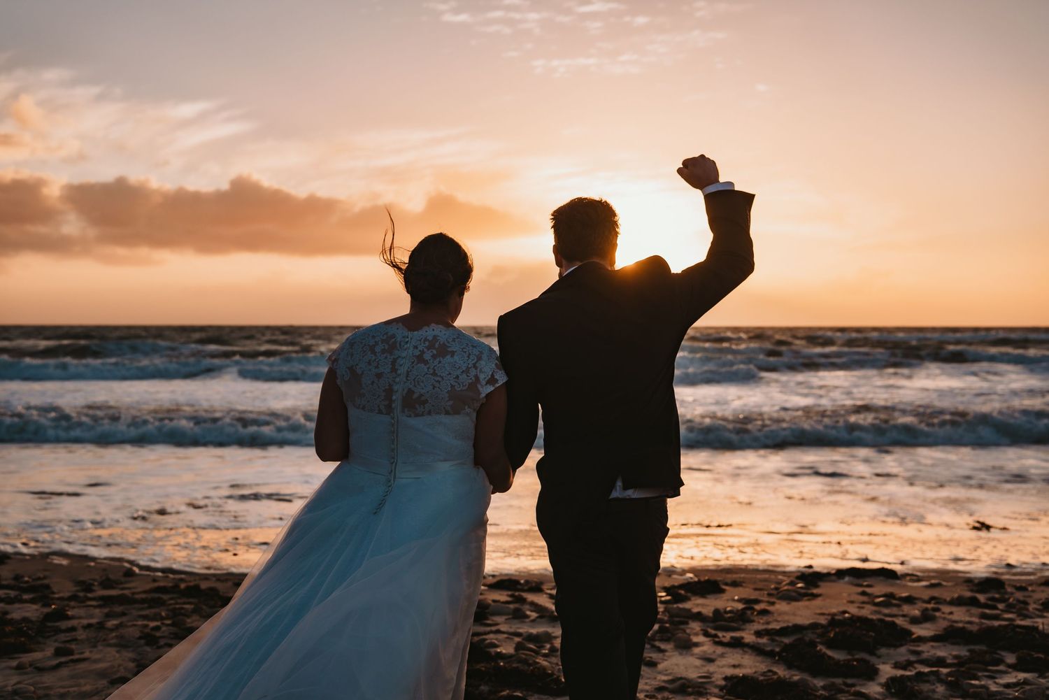 Silhouetted couple celebrating on beach at sunset with waves crashing in background.
