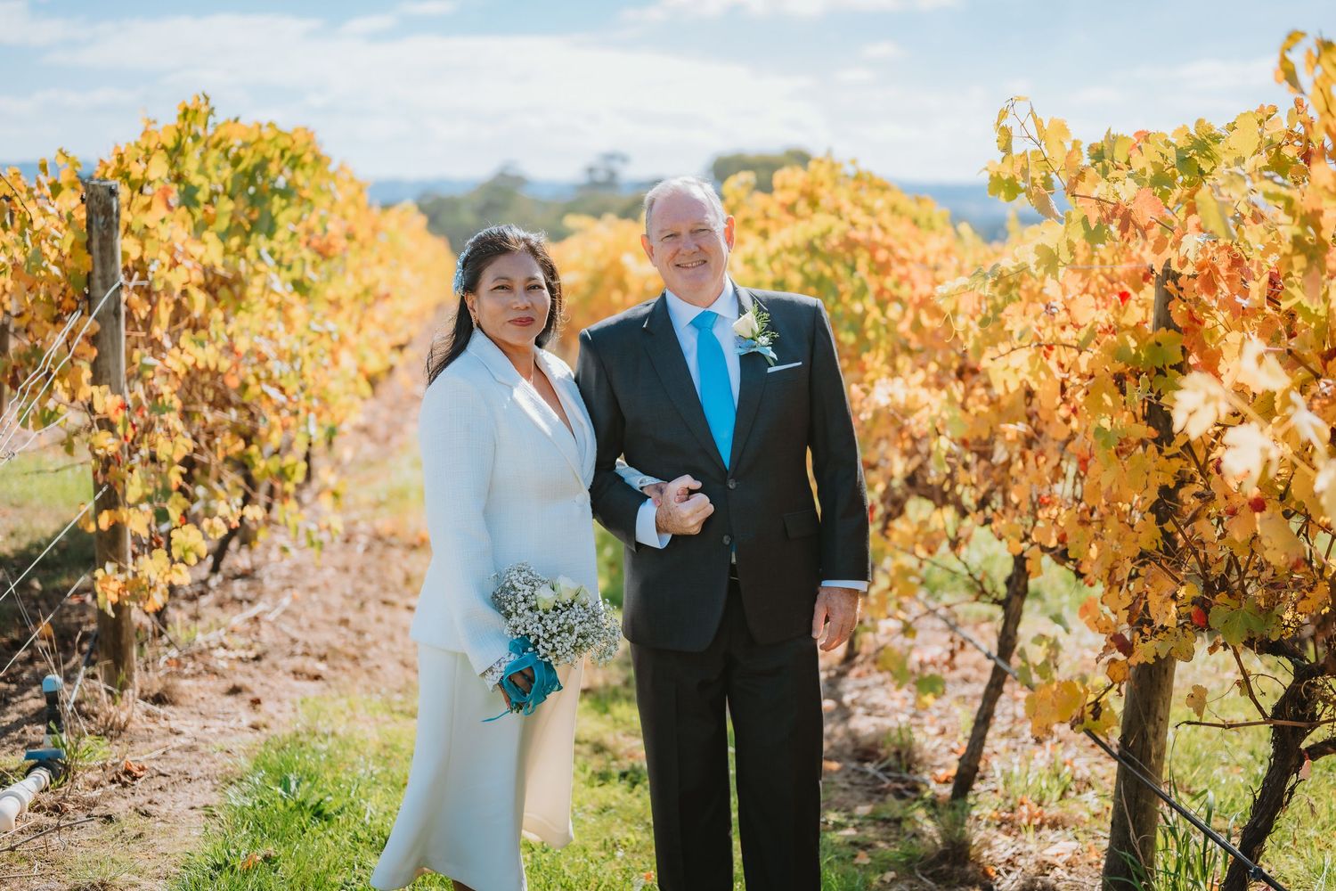 A couple poses together in a vineyard during autumn with colorful fall foliage and golden light.