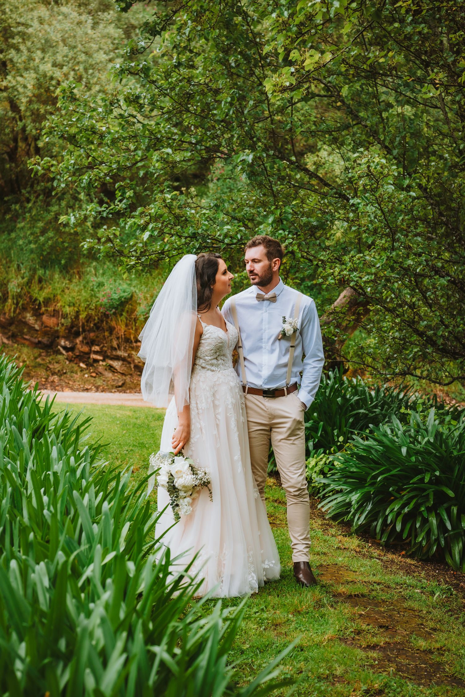 A romantic outdoor garden wedding photo showing a couple on a path lined with lush greenery and irises.