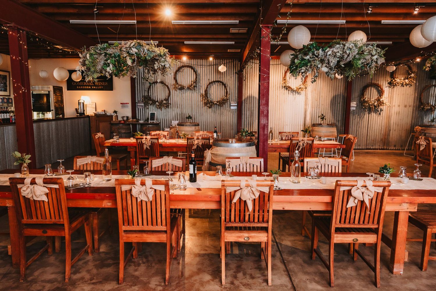 Rustic restaurant dining room decorated with wooden chairs, hanging greenery and wreaths in warm lighting atmosphere.