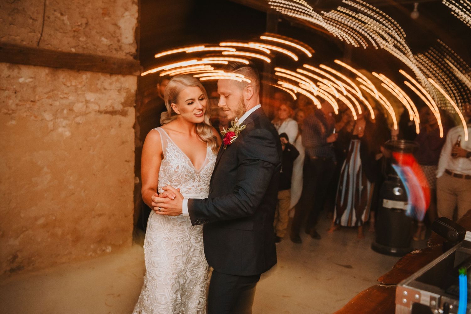 A couple celebrates their first dance at a rustic wedding venue with light trails creating magical streaks in the background.