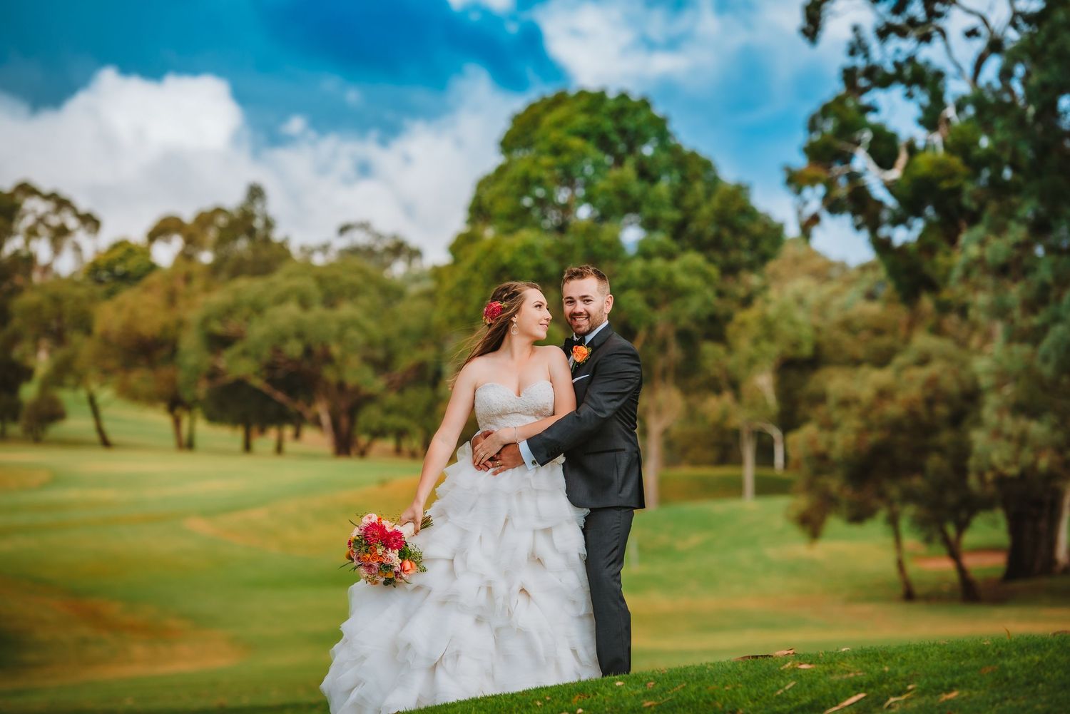 A couple in wedding attire share a joyful moment together on a lush green golf course with trees in the background.