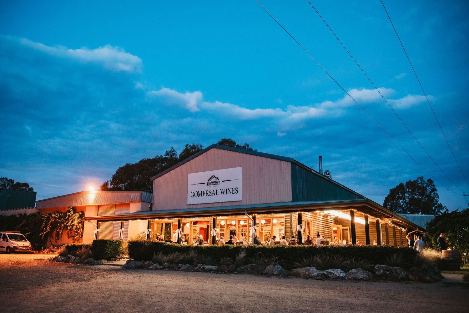 A rustic country store glows warmly at dusk under a deep blue sky with power lines overhead.