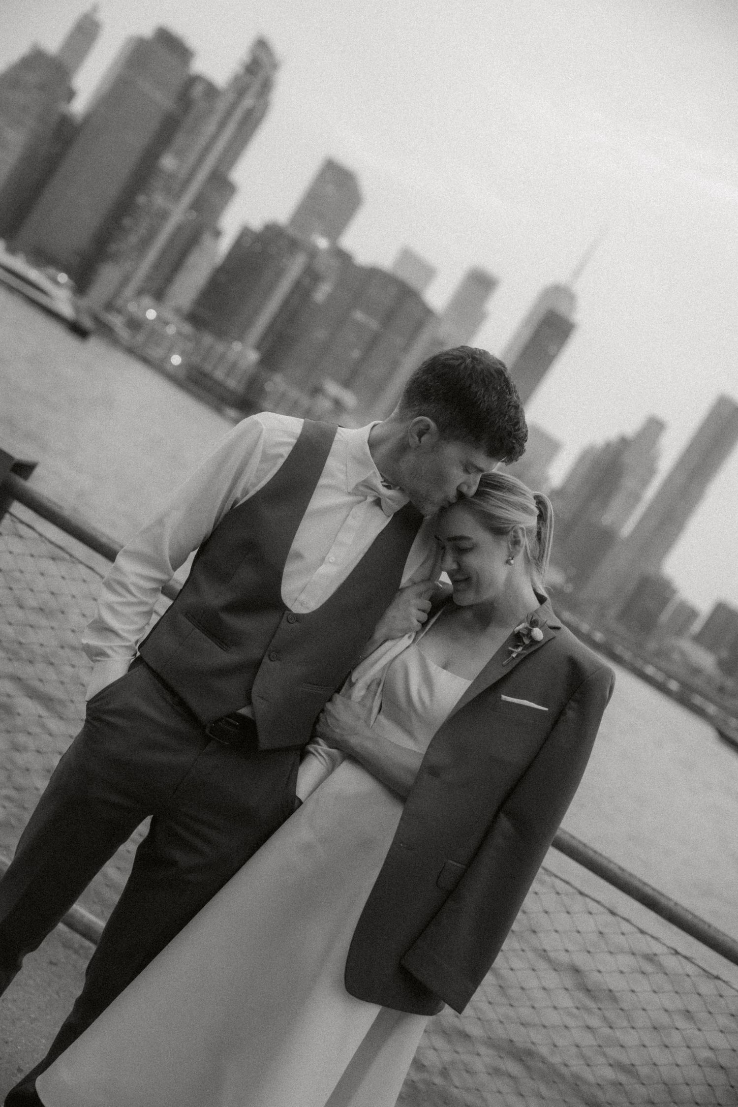 A romantic couple embraces against a cityscape backdrop in a series of black and white photographs.