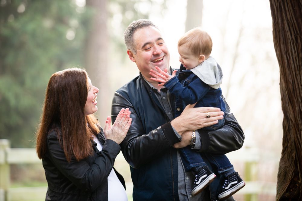 Playful family portrait session outdoors with natural lighting and trees.