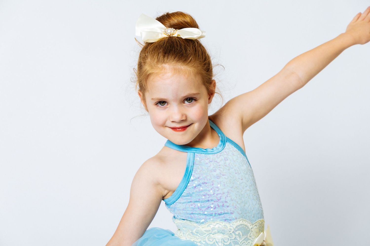 Young red-haired girl in blue sequin dance costume striking a pose with arm raised.