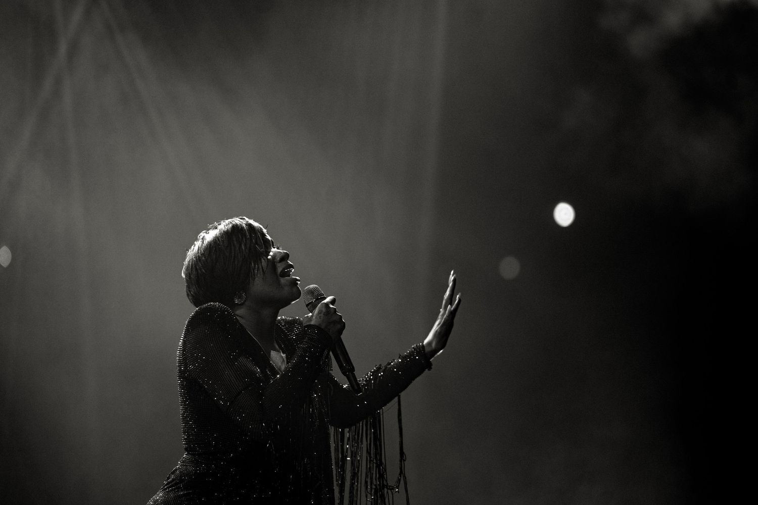 Black and white photo of a singer performing on stage with dramatic lighting and raised hand.
