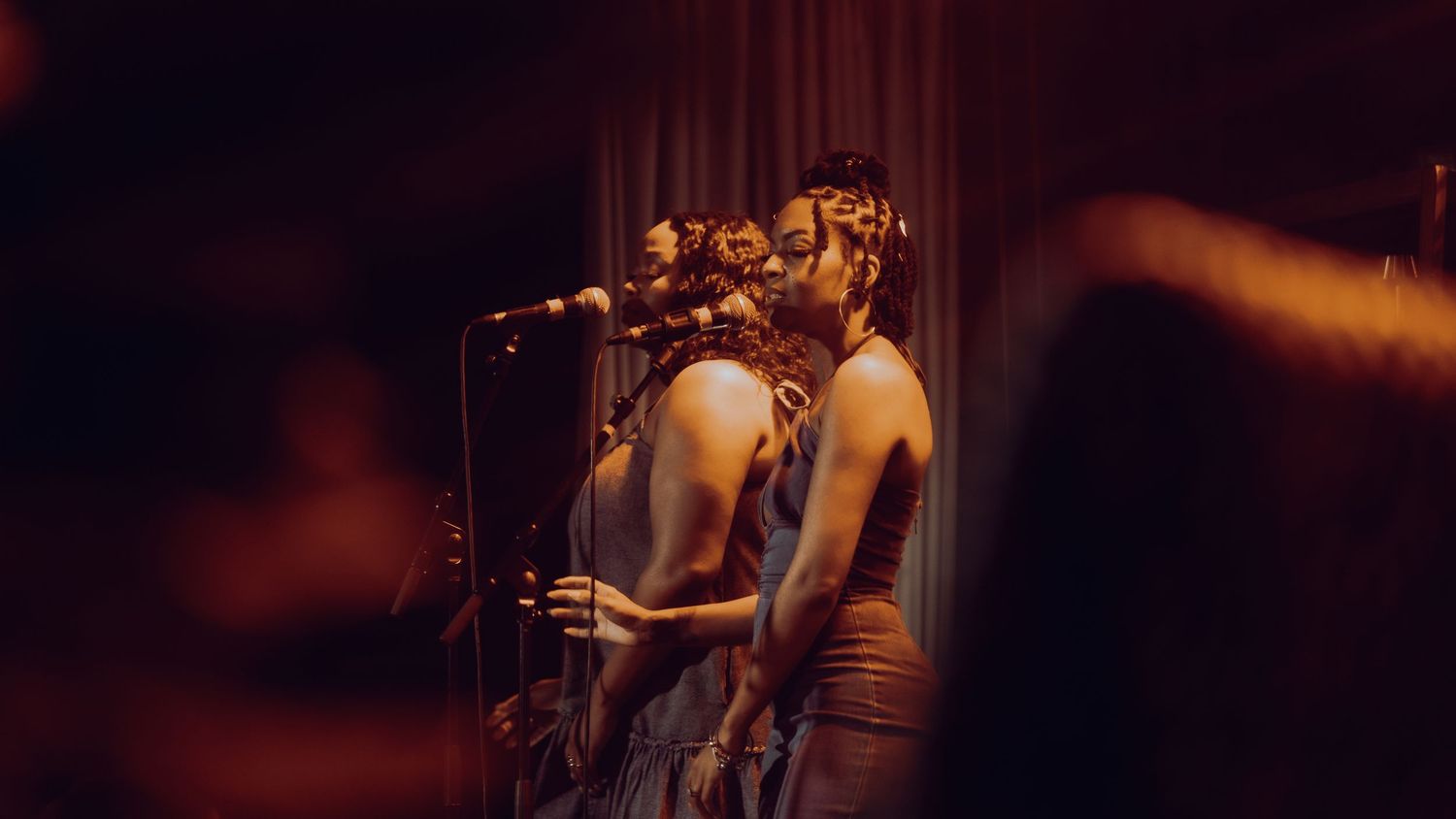 A female vocalist performs at a microphone stand in moody amber stage lighting.