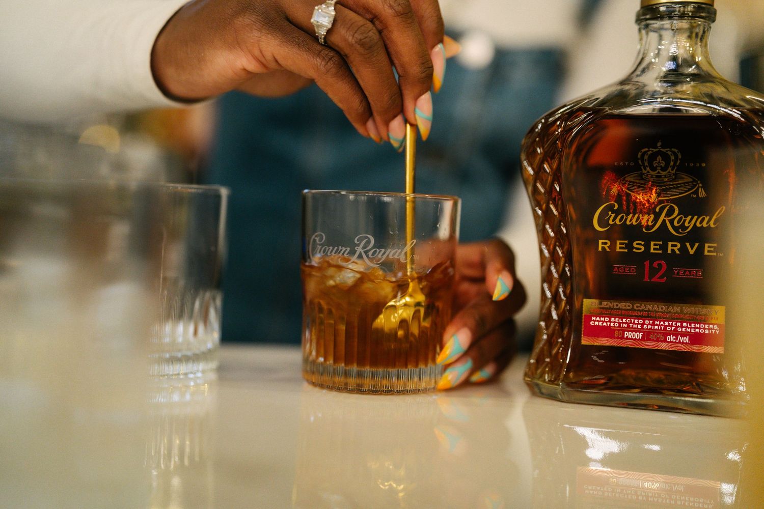 Crown Royal Reserve 12 whiskey being stirred in a rocks glass on a bar.