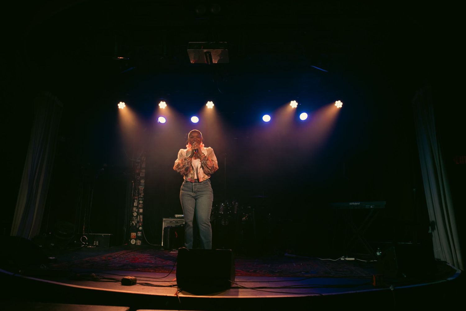Solo performer on stage under colorful blue and yellow spotlights in a dark concert venue.