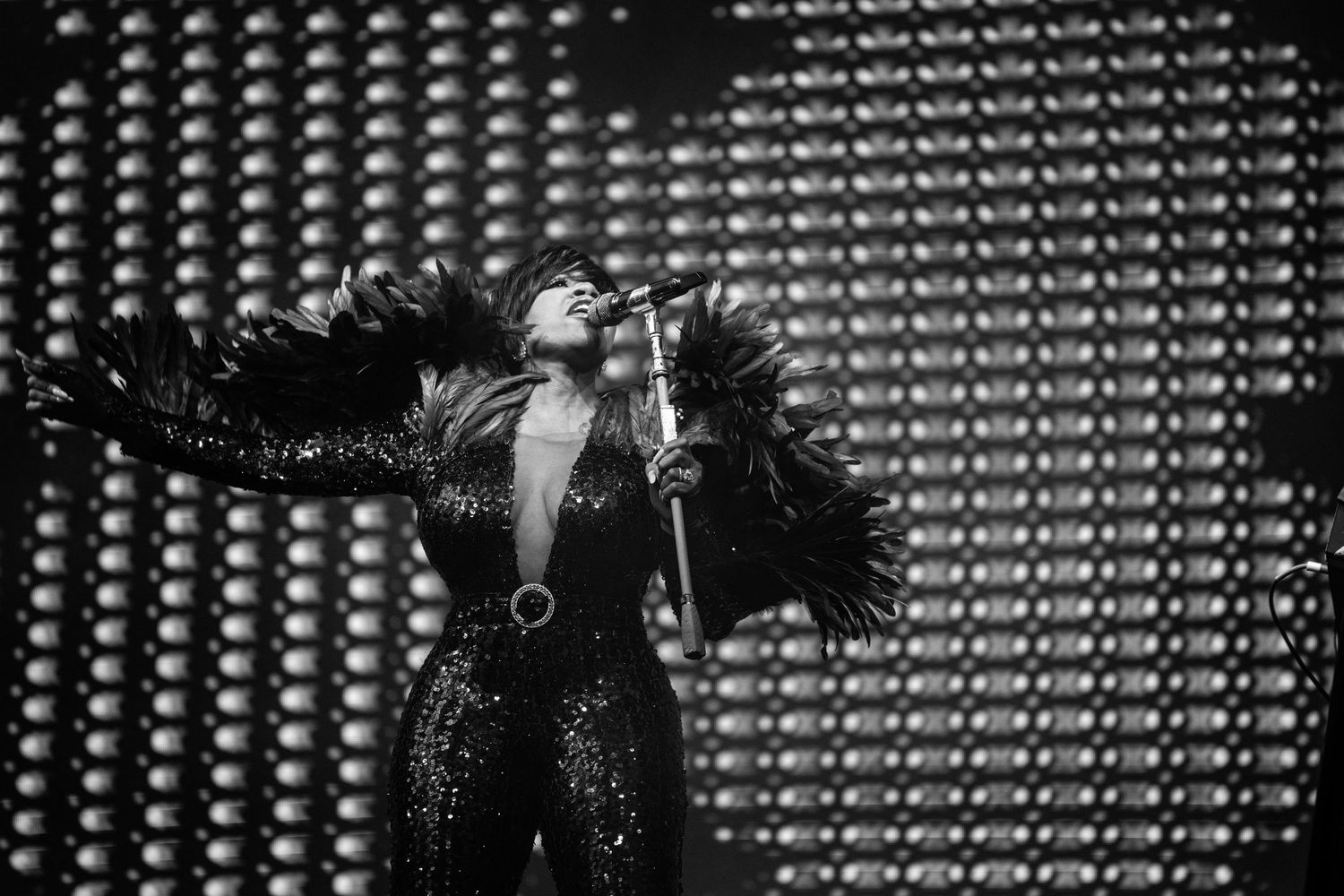Black and white photo of a female performer in feathered costume singing on stage with dramatic lighting.