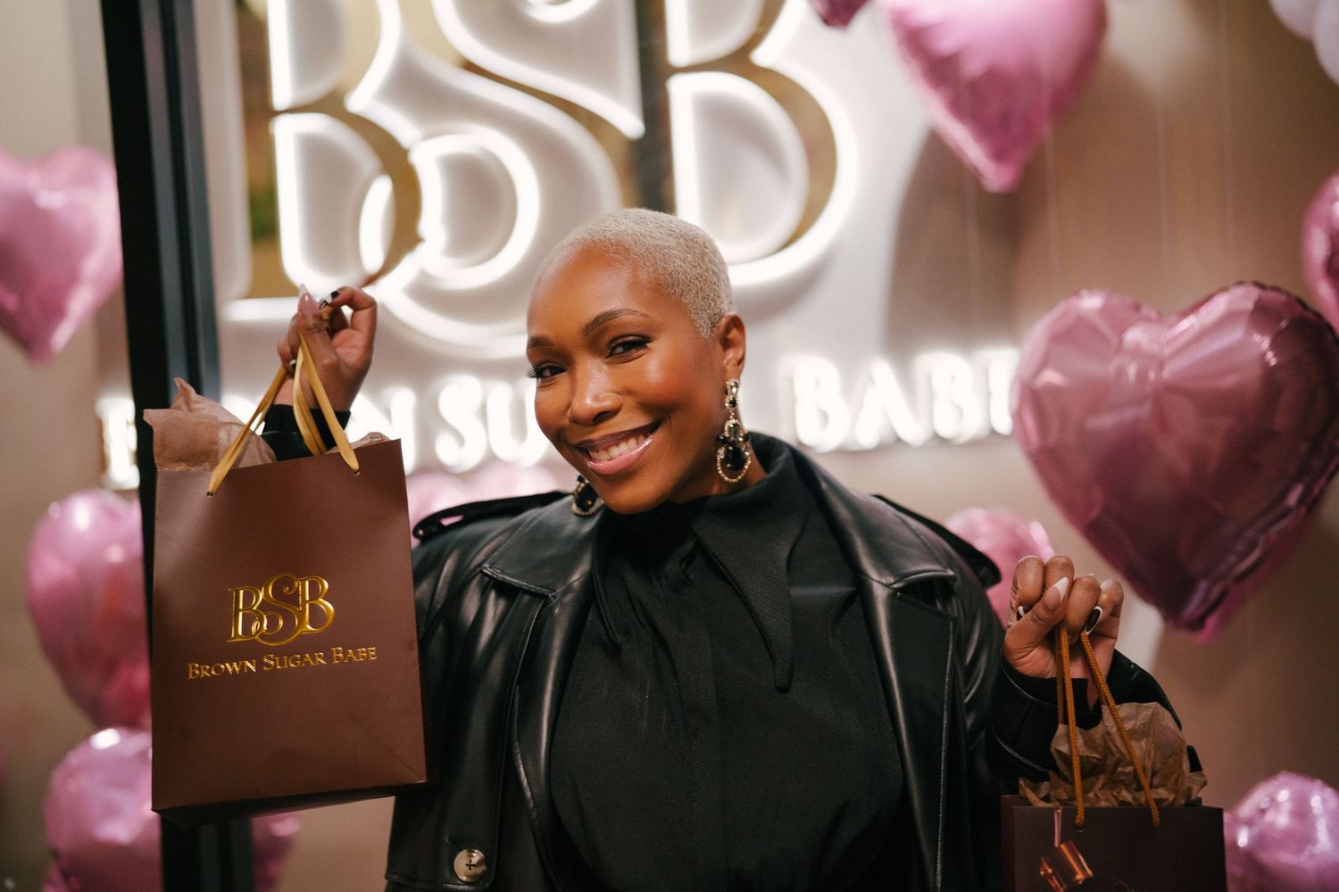 Woman smiling at BSB store event, holding shopping bags surrounded by pink heart balloons.