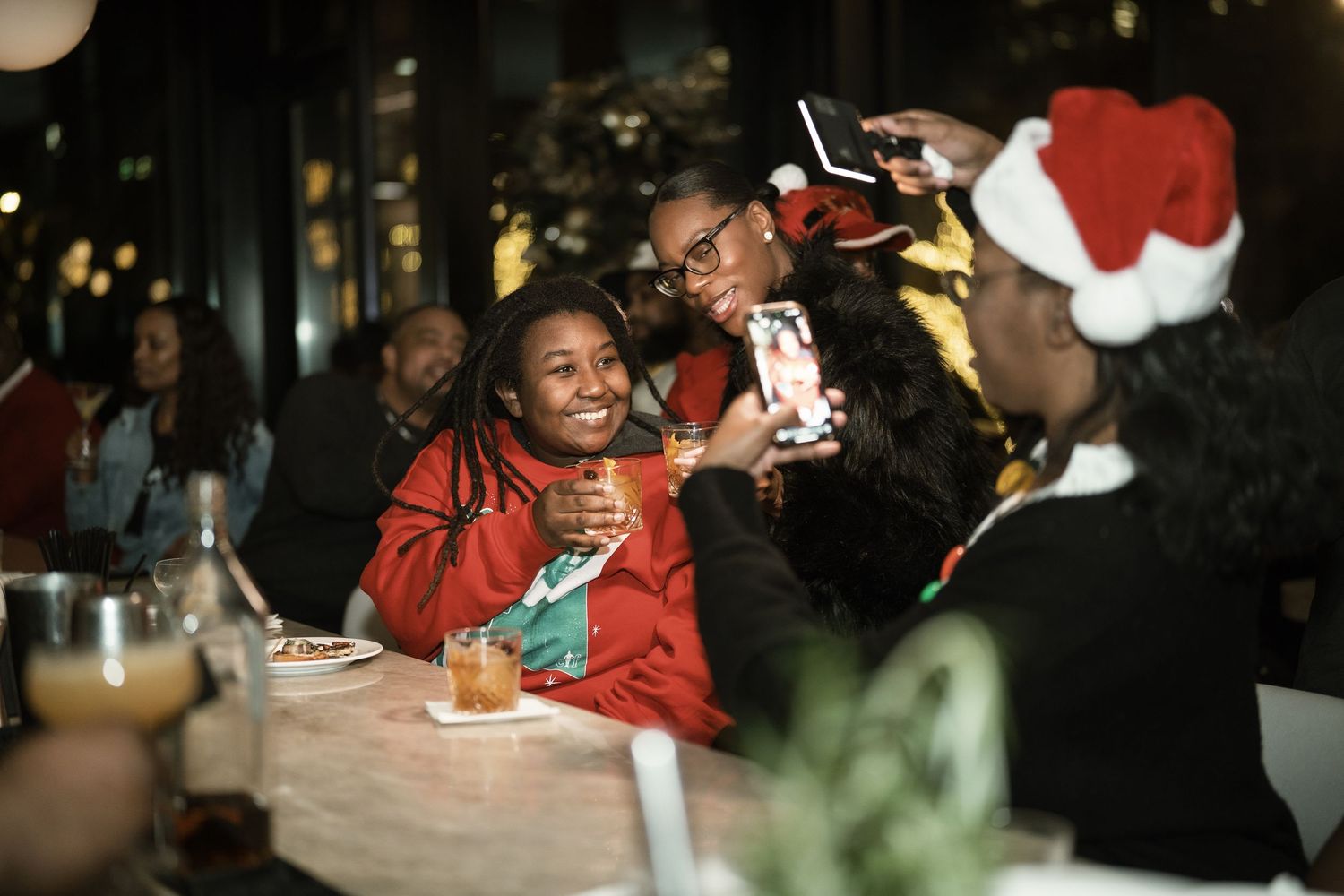 Students smile and engage in lively conversation while enjoying a meal together in a dimly lit dining setting.