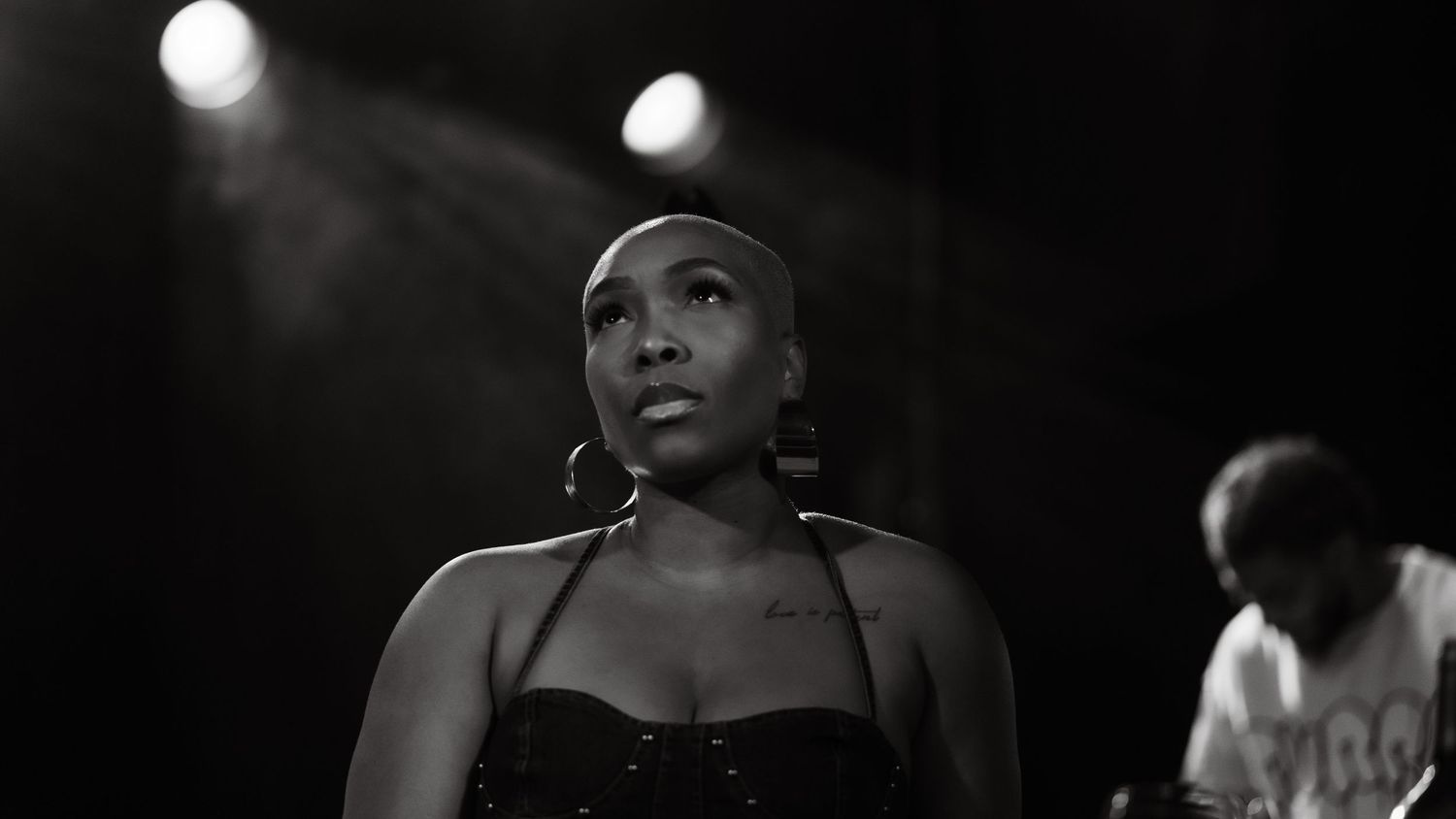 Black and white portrait of female singer on stage wearing black dress with hoop earrings.