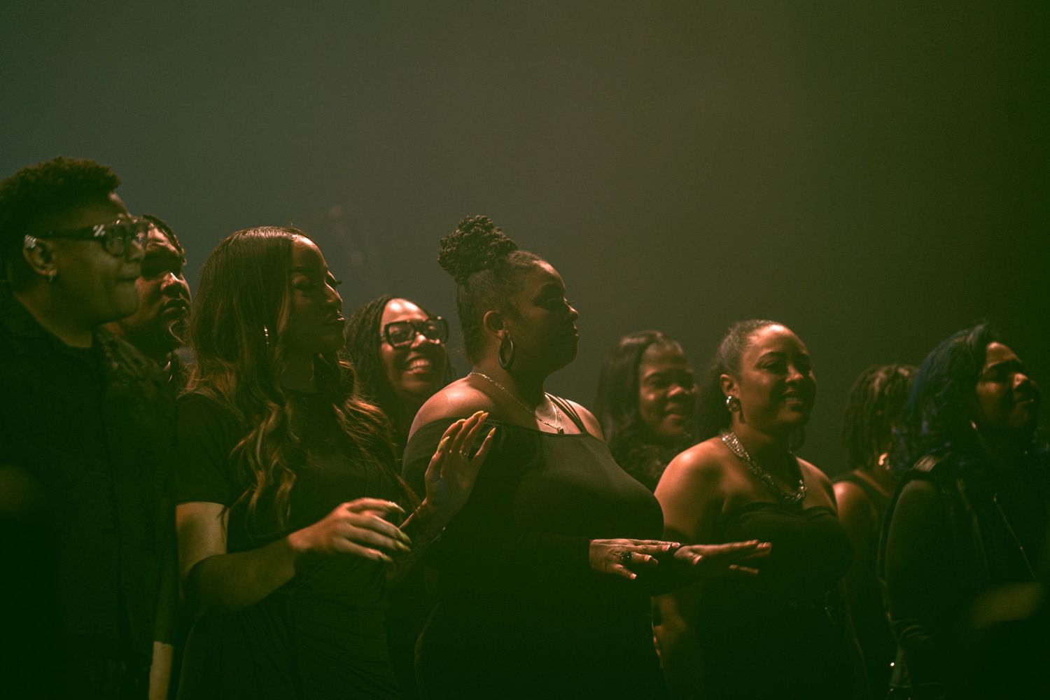 A diverse group of joyful people smiling and laughing together at a live music event in dim lighting.