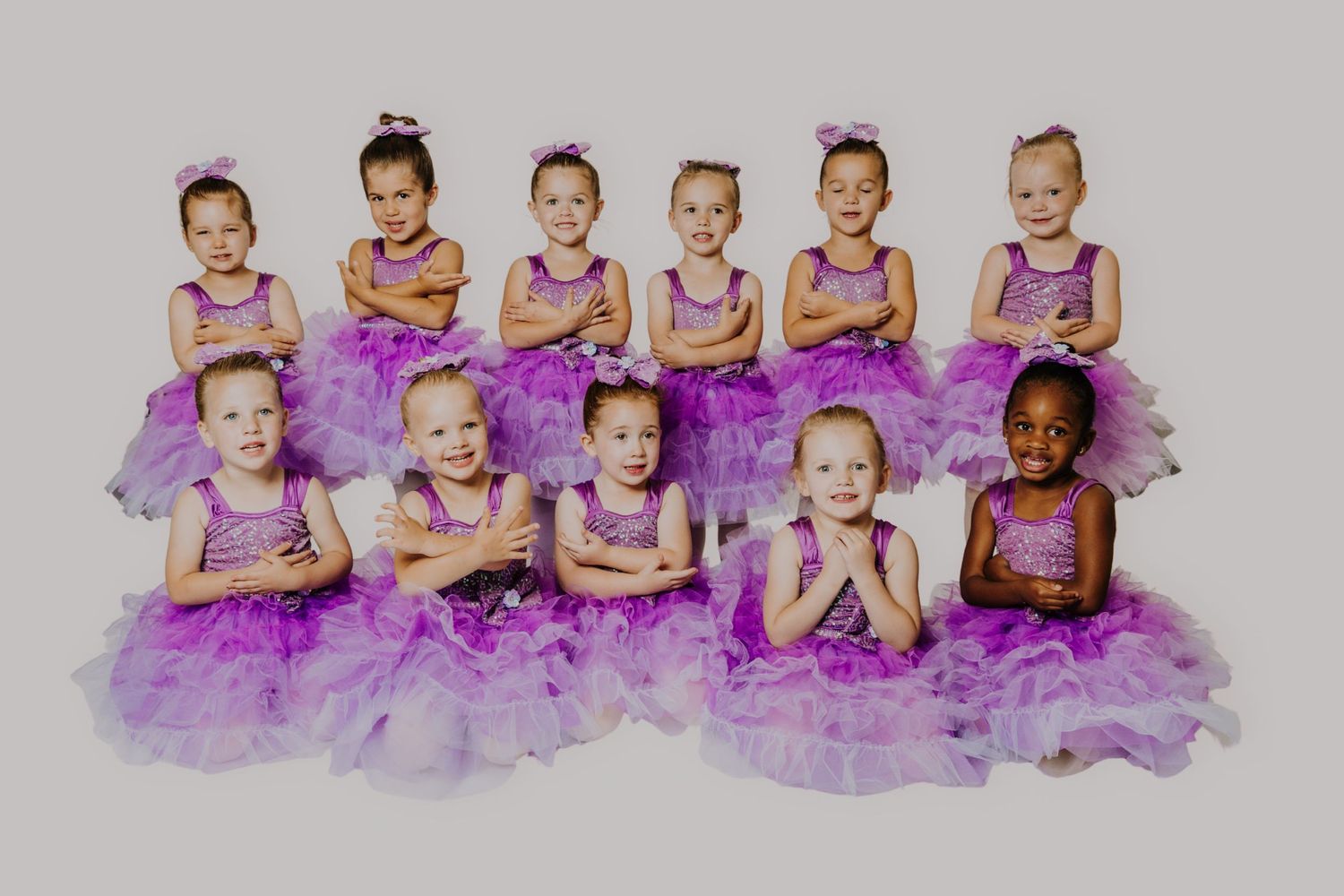Group of young girls in matching purple tutu dresses posing together for a dance recital photo.