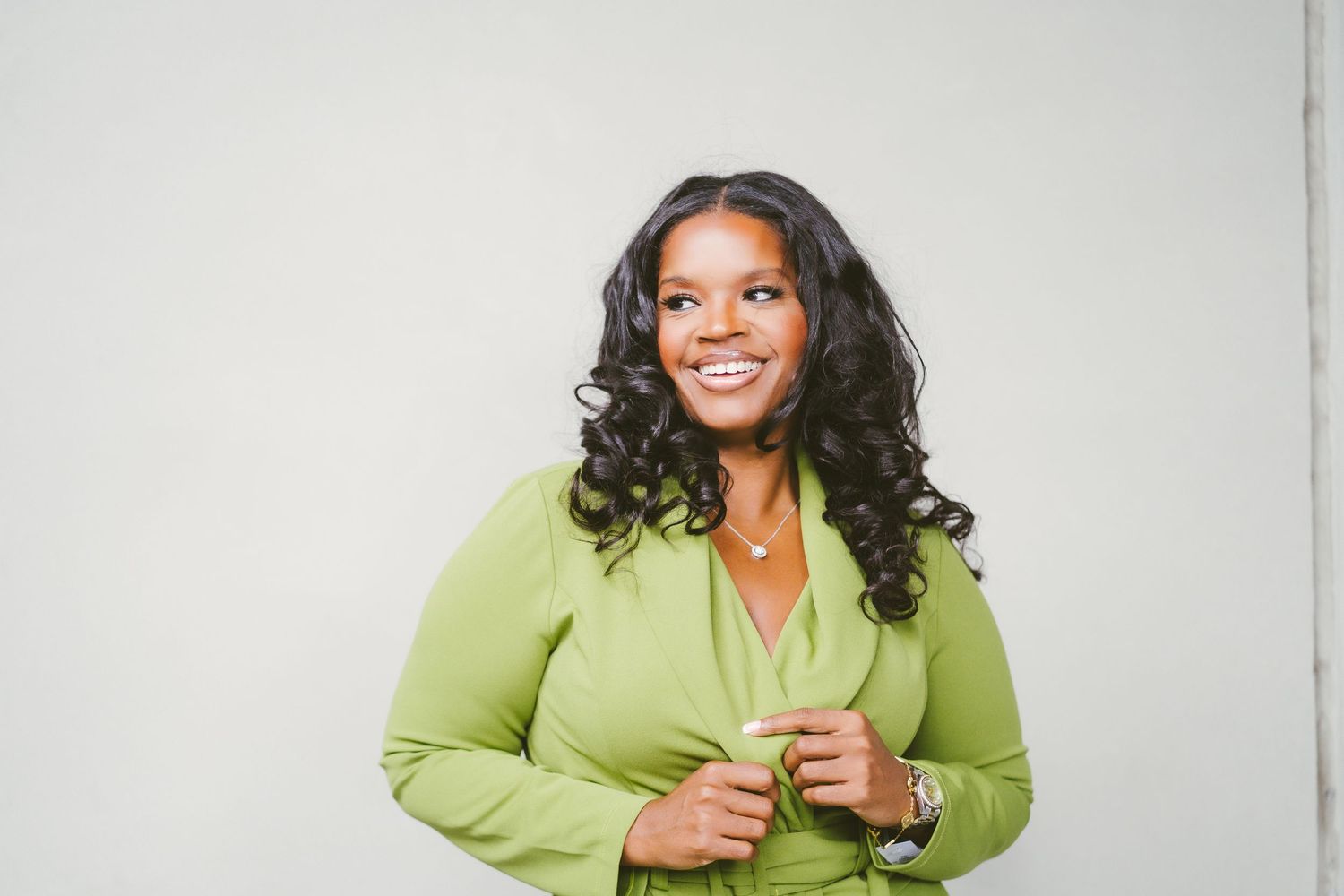 Studio portrait of person in lime green blazer with curled hair and joyful expression.