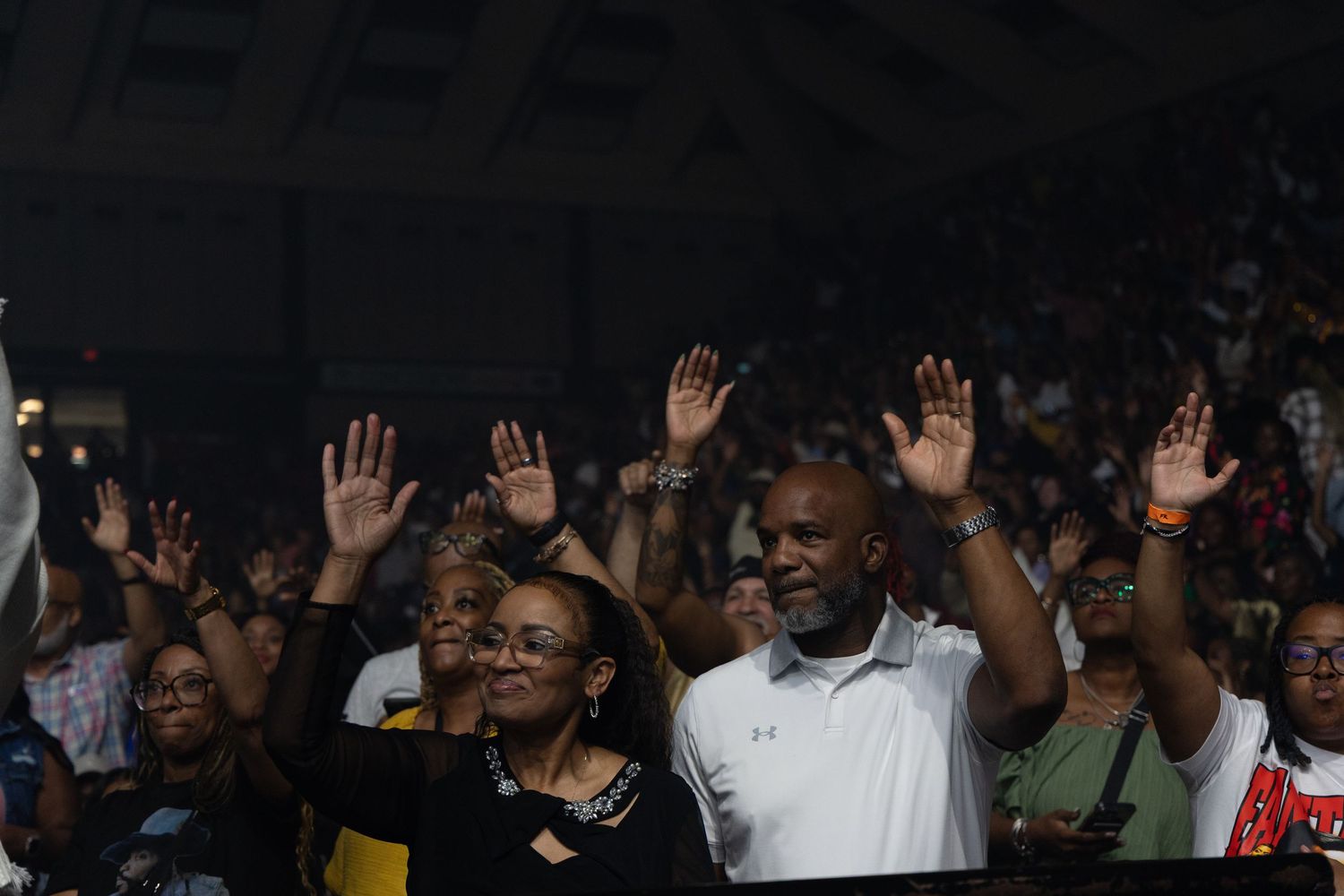 Crowd of people raising hands at a live concert event in a packed indoor arena.