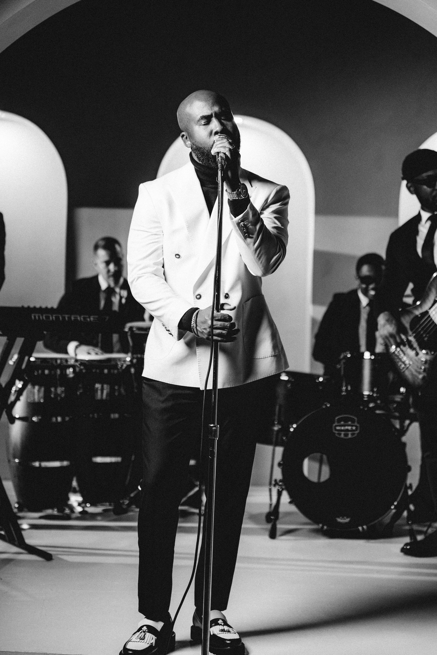 Black and white performance photo of musicians on stage with dramatic lighting.