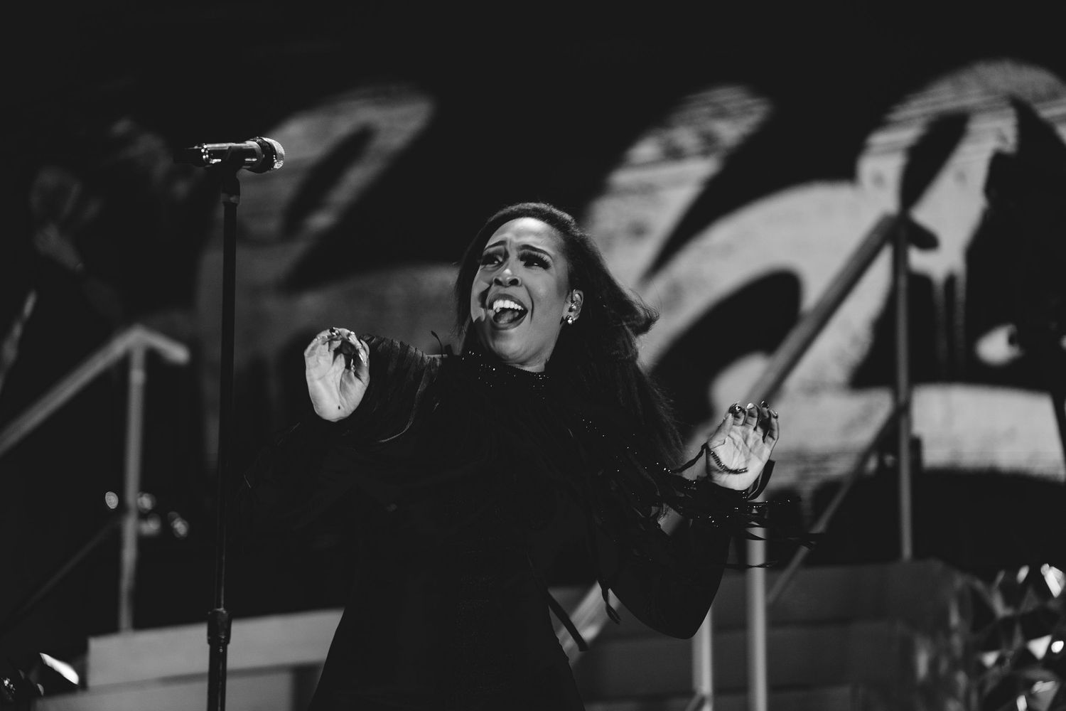 Black and white photo of a female singer performing passionately on stage with microphone and dramatic backdrop.