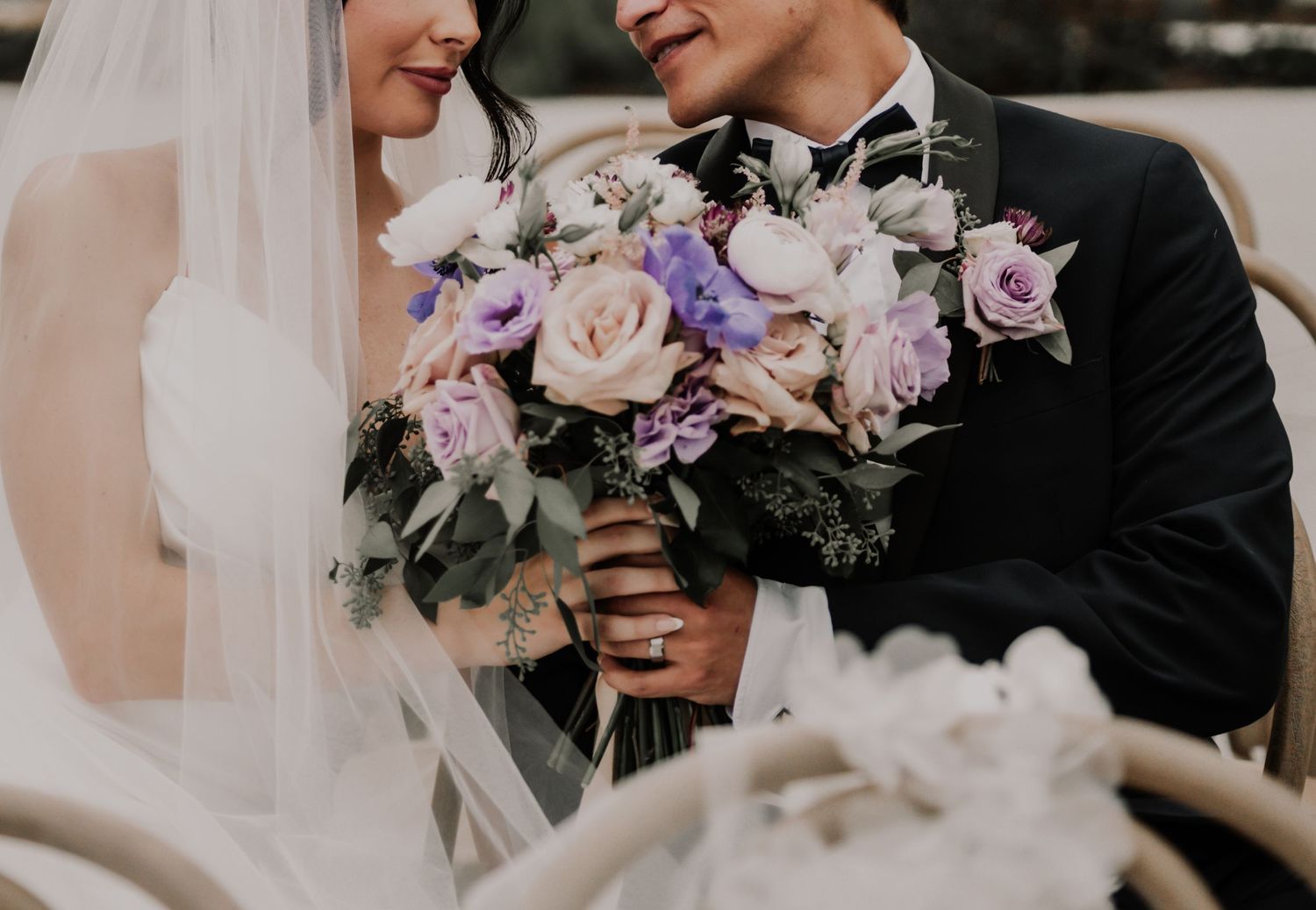 A couple holds beautiful purple and pink floral bouquets at an elegant wedding ceremony.