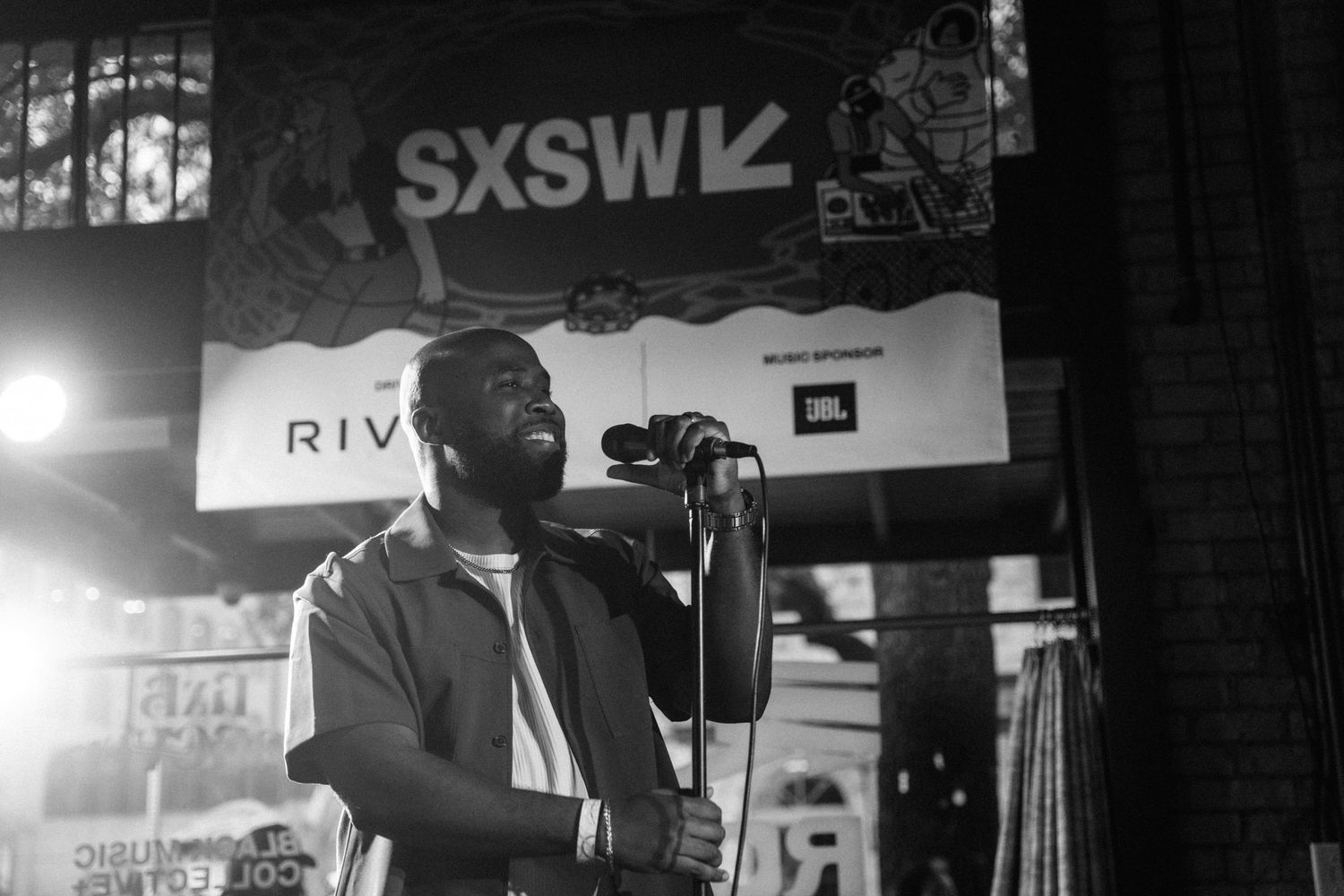 Black and white photo of a performer singing at SXSW music festival on an outdoor stage with JBL speakers.