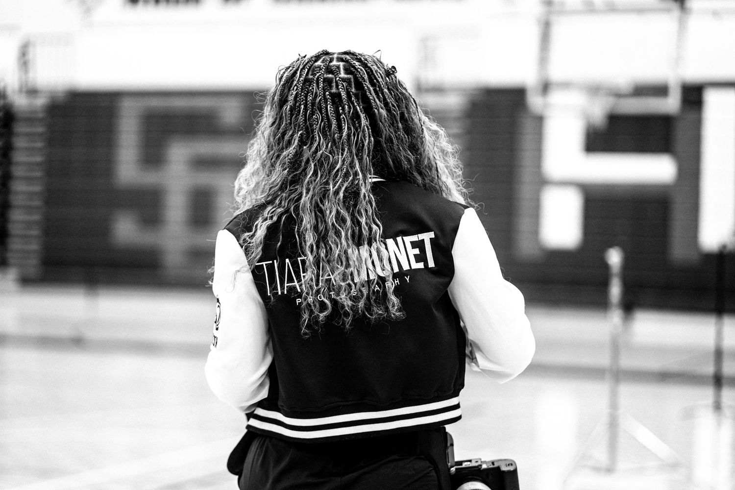 Back view of someone wearing a varsity jacket with text in a gymnasium.