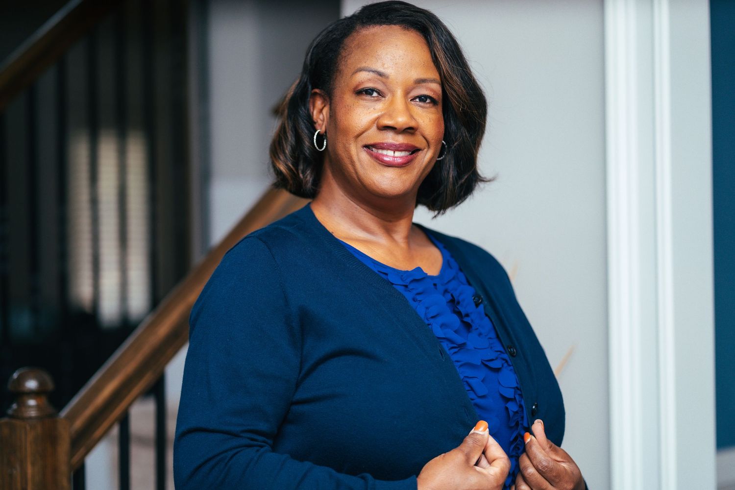 Professional portrait of someone wearing a navy blazer and royal blue ruffled top against a light background.