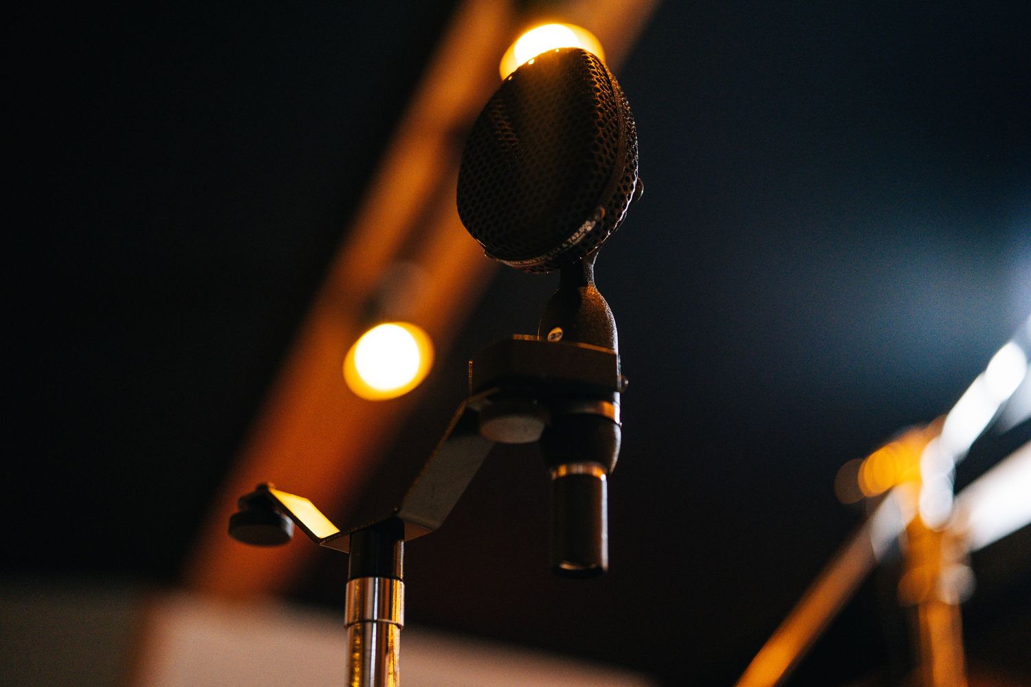 Close-up of a professional condenser microphone on a stand in a dimly lit recording studio with warm bokeh lights.