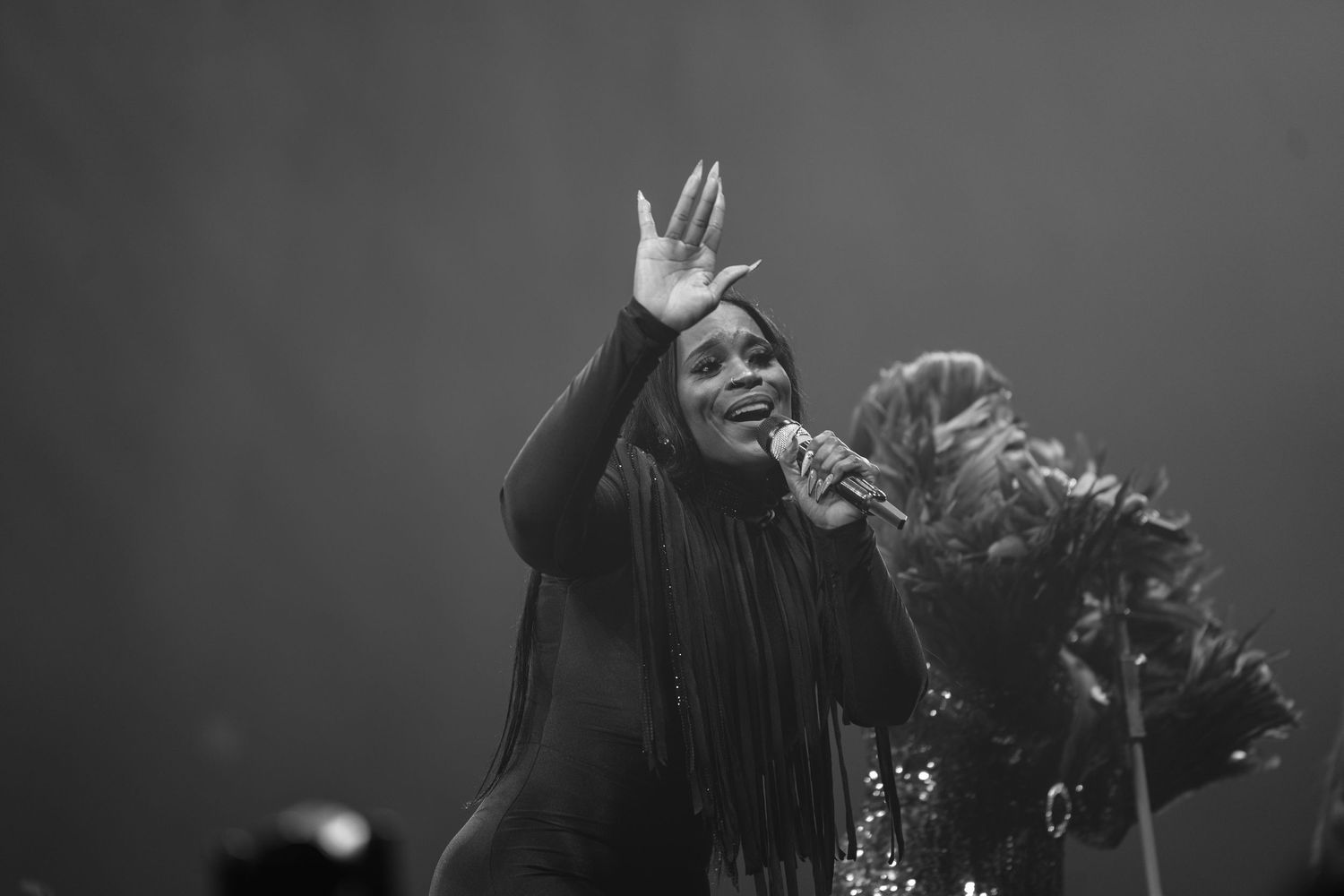 Black and white concert photo of a female singer waving to the crowd on stage.