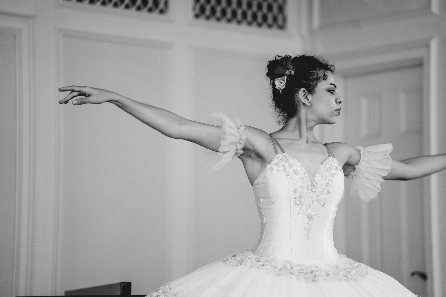Black and white photo of a graceful ballerina in a white tutu performing an elegant pose with arms extended.