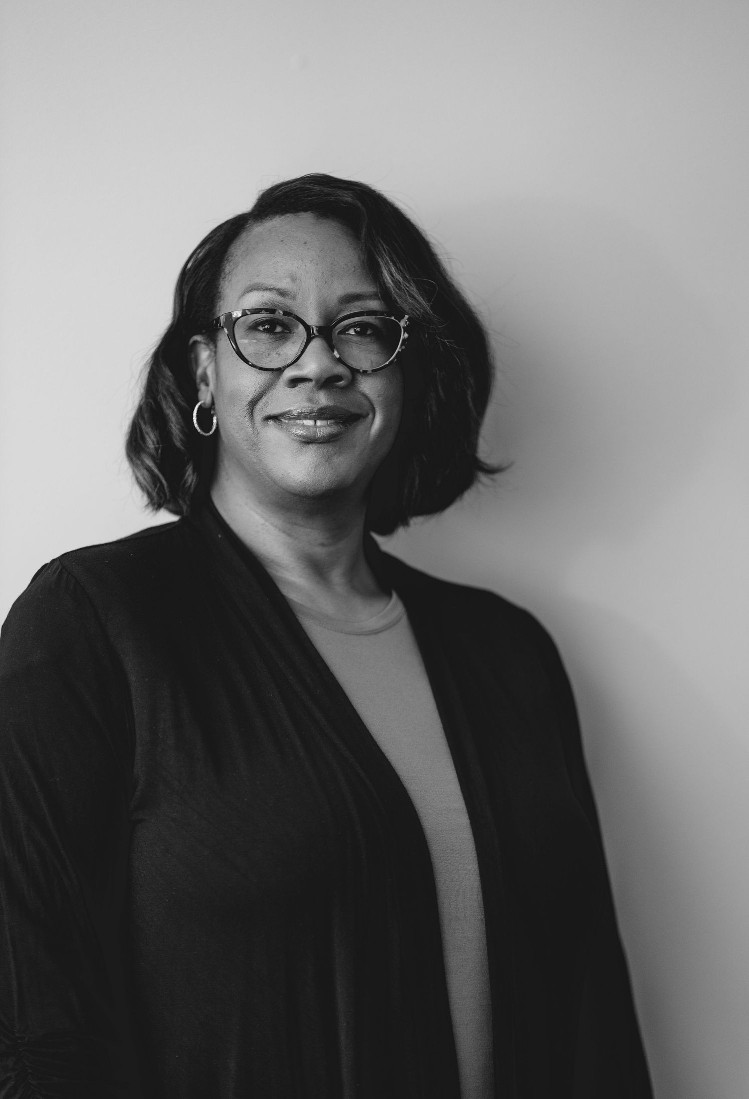 Black and white professional portrait showing someone in glasses and dark blazer.