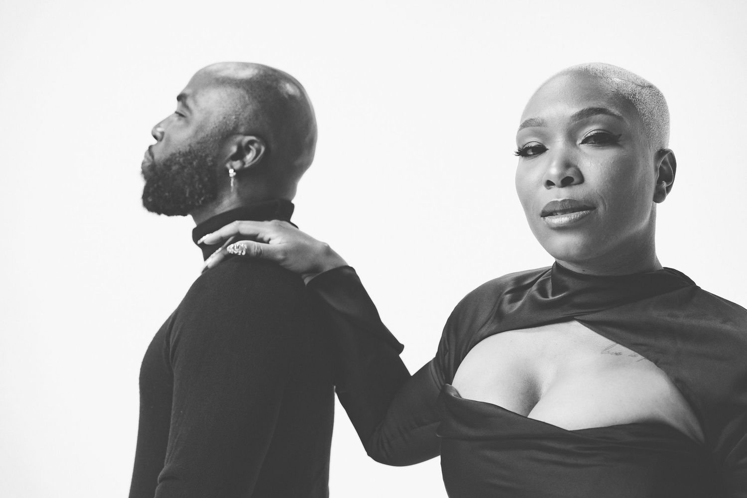 Artistic black and white portrait of two people in an intimate pose against white background.