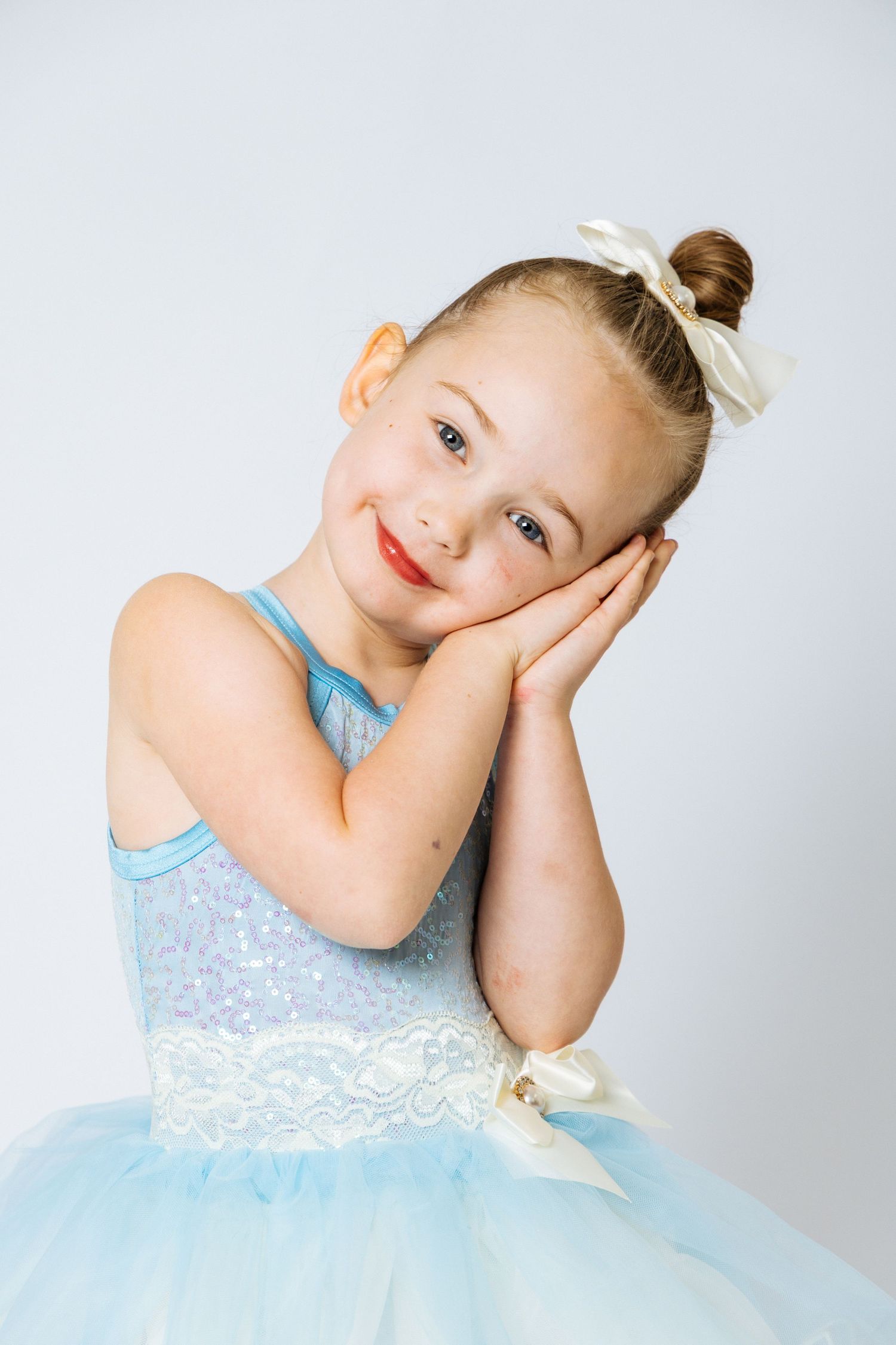 Cute little girl in blue tutu ballet dress posing with hands on cheeks, smiling.