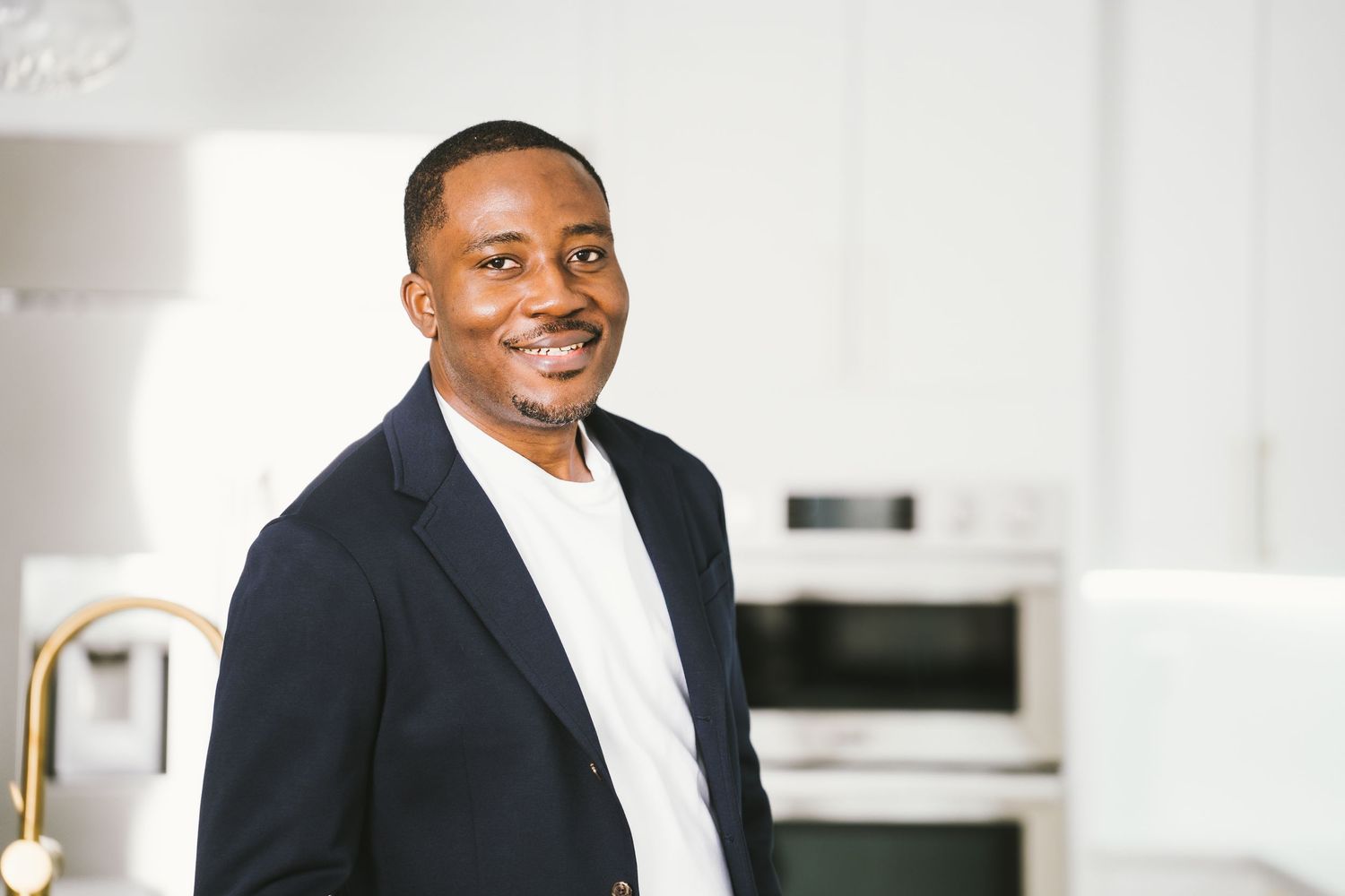 Professional in a dark suit smiles warmly while standing in a bright modern office setting.