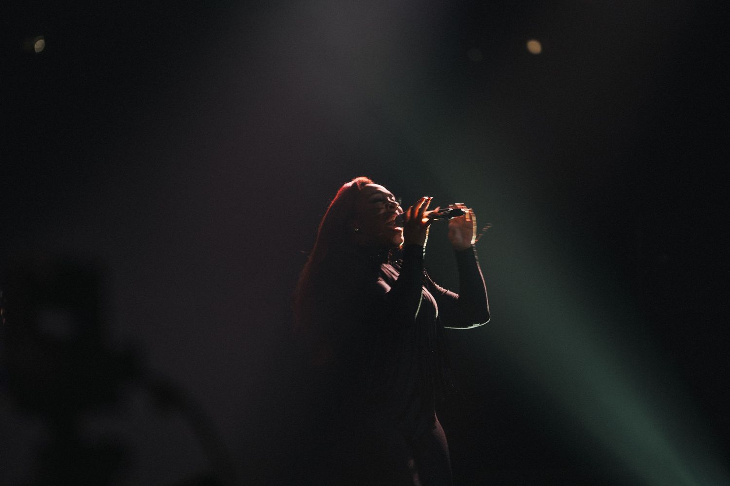 A singer performing on stage under dramatic spotlights in a dark concert venue.