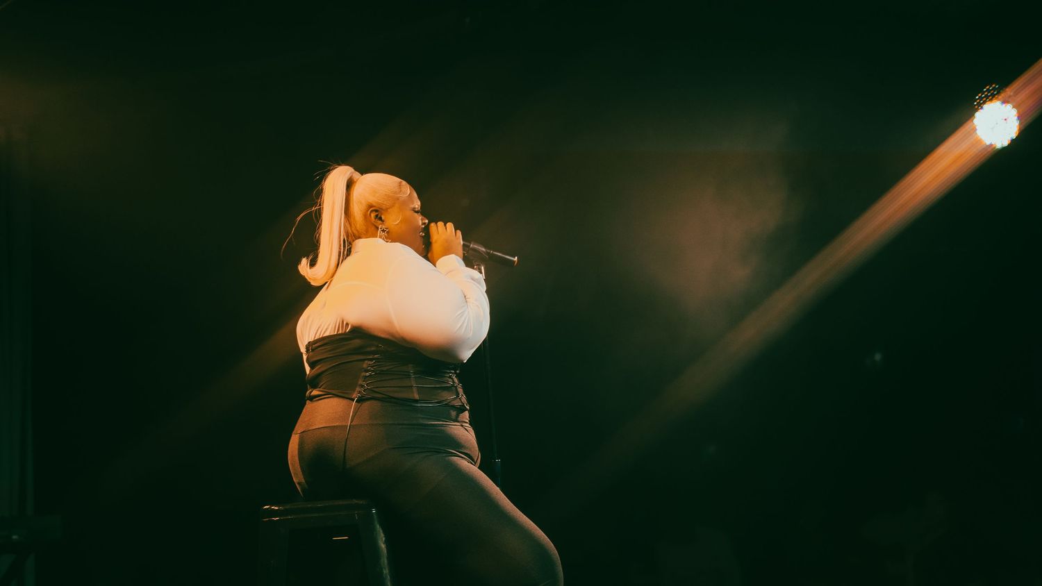 Female singer performing on stage with microphone, dramatic spotlight beams cutting through dark atmosphere.