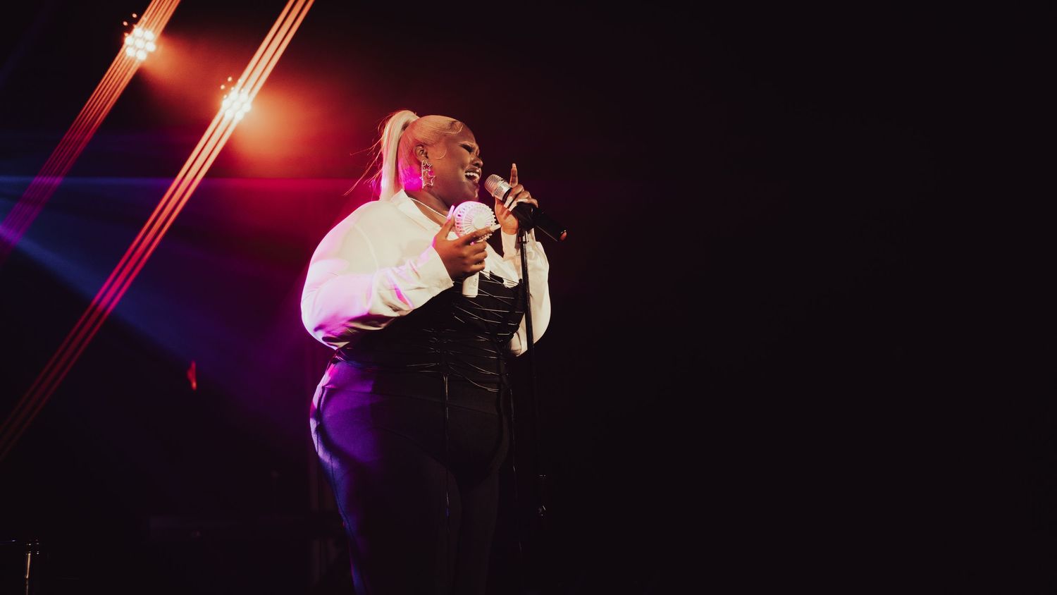 Female vocalist performing on stage in white and black outfit under dramatic red and purple stage lights.