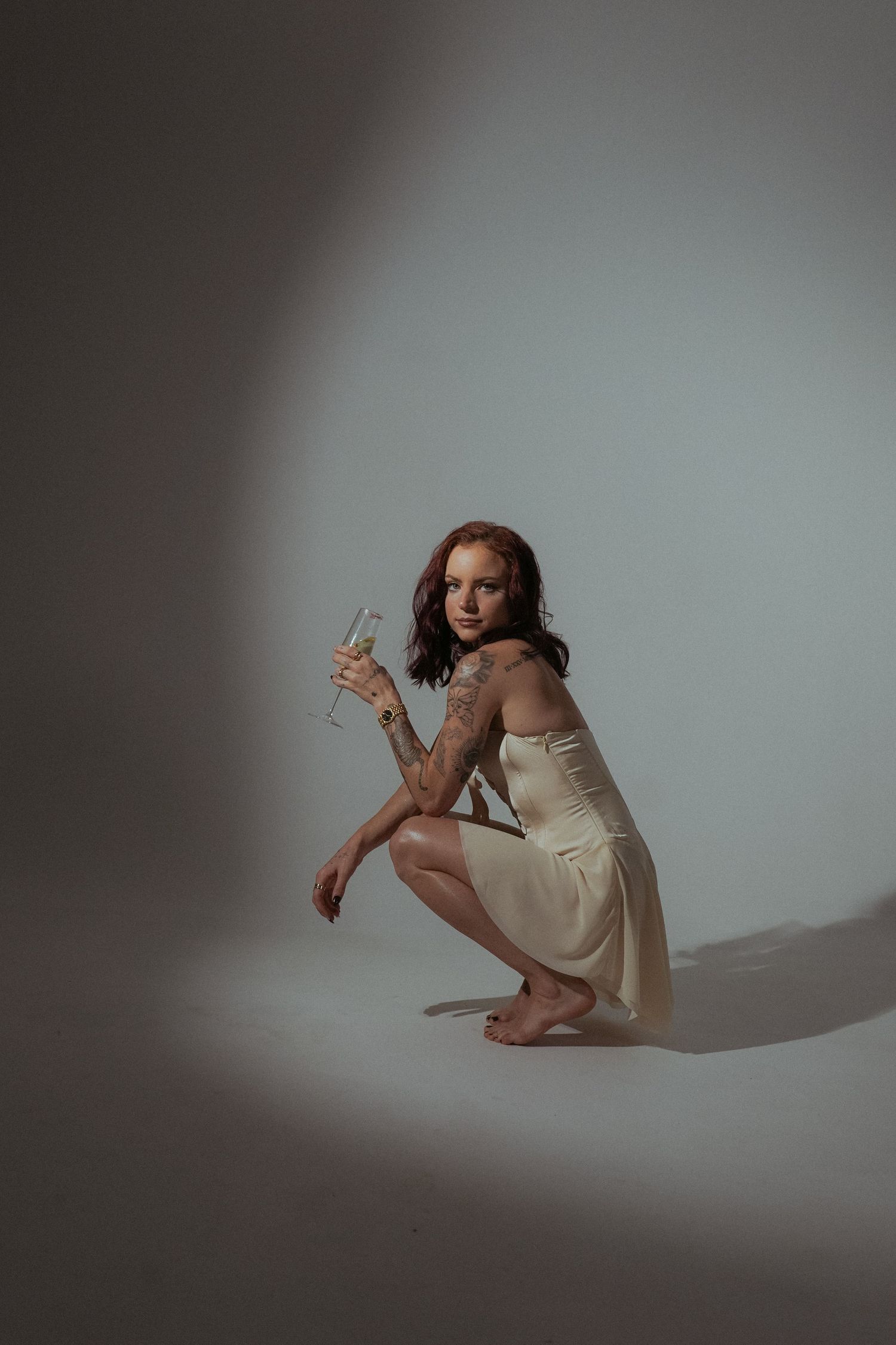 Artistic portrait in cream dress holding champagne glass in spotlight.