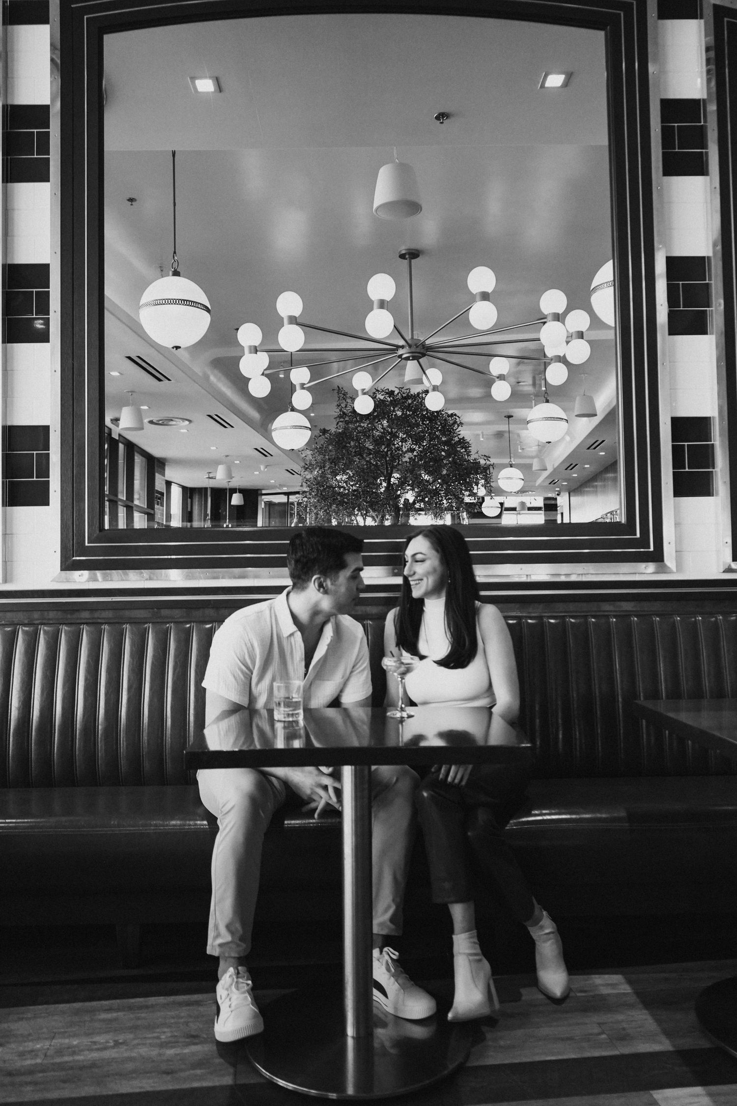 A couple shares a romantic moment in a retro diner booth reflected in a large mirror.