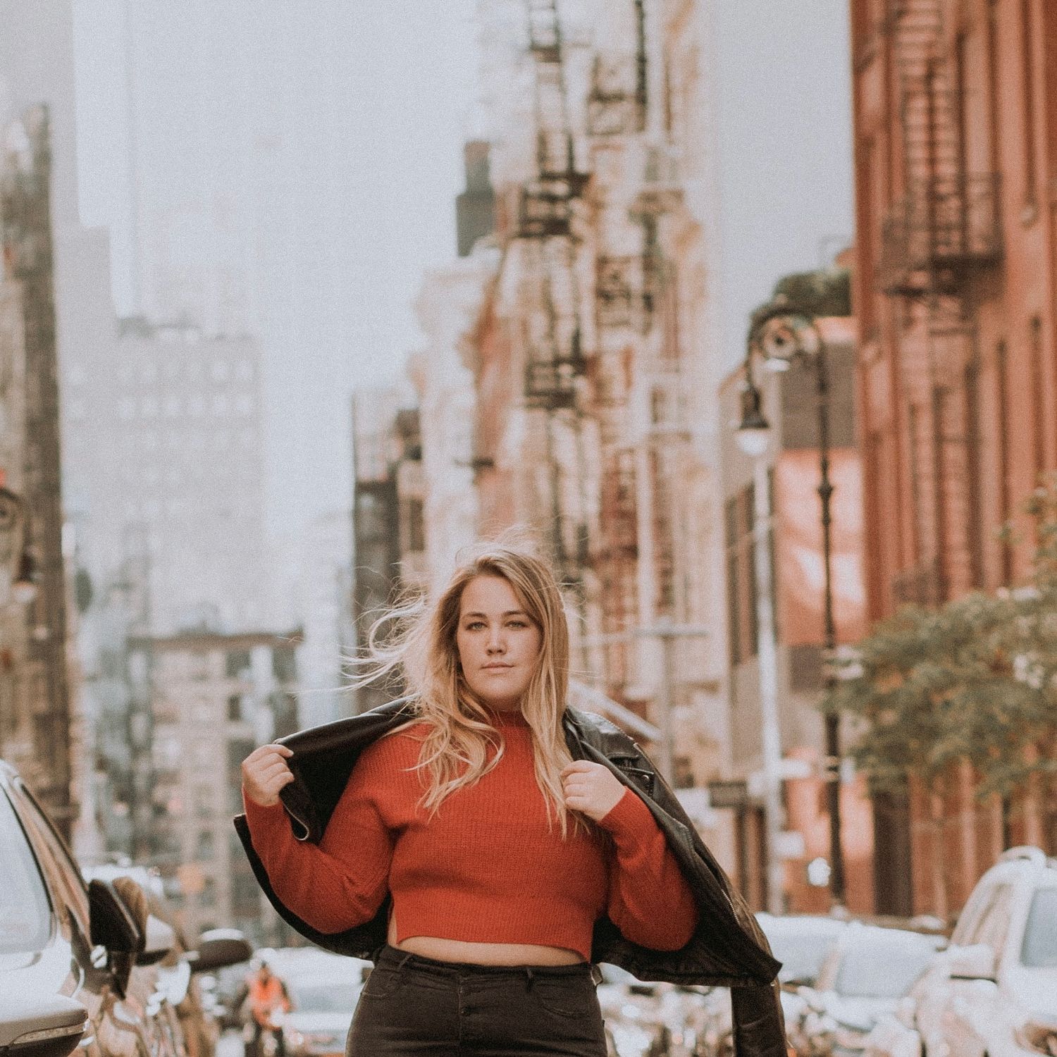Woman in red crop top and jacket posing confidently on urban New York City street.