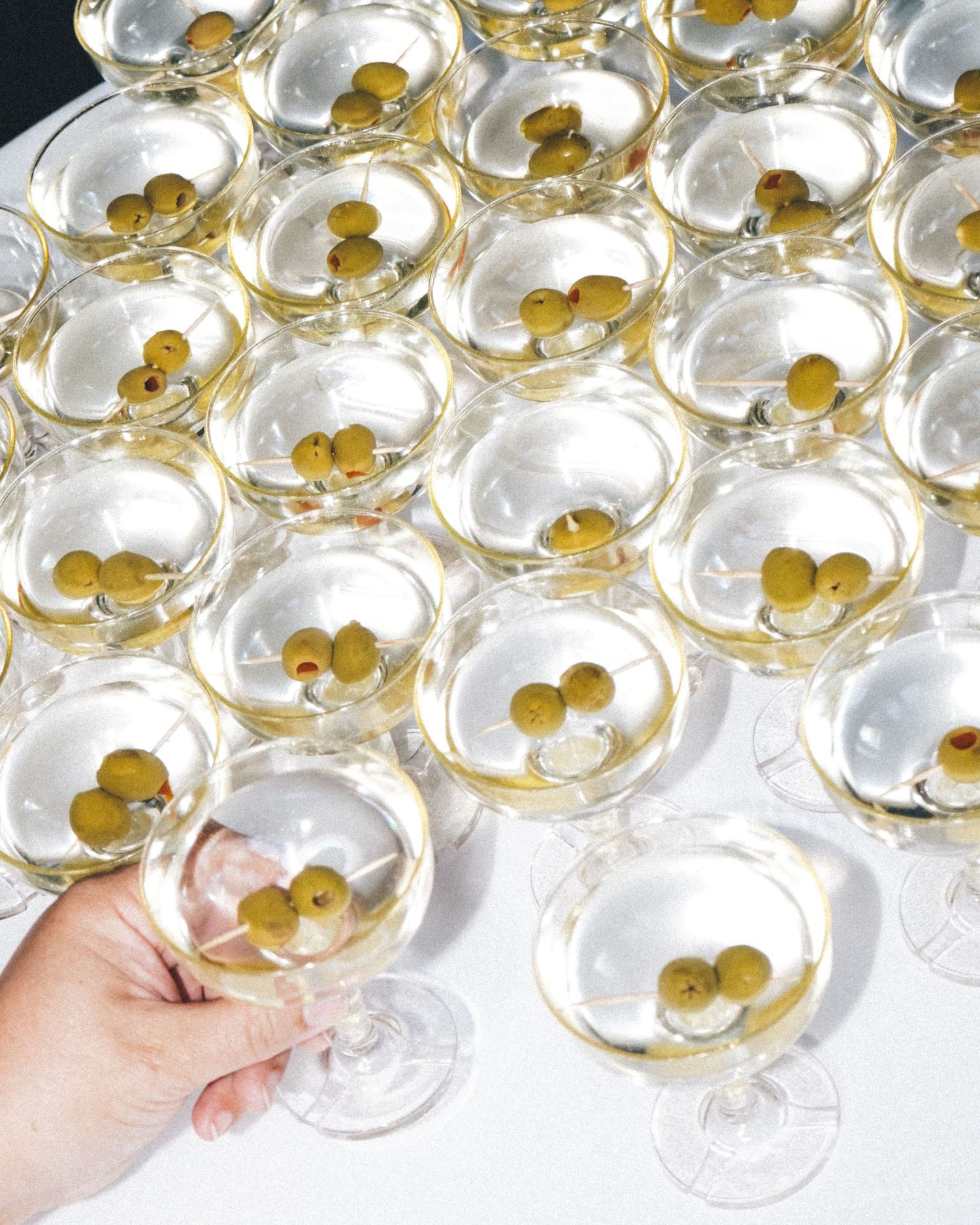 Multiple champagne coupes with gold olives arranged in a geometric pattern.