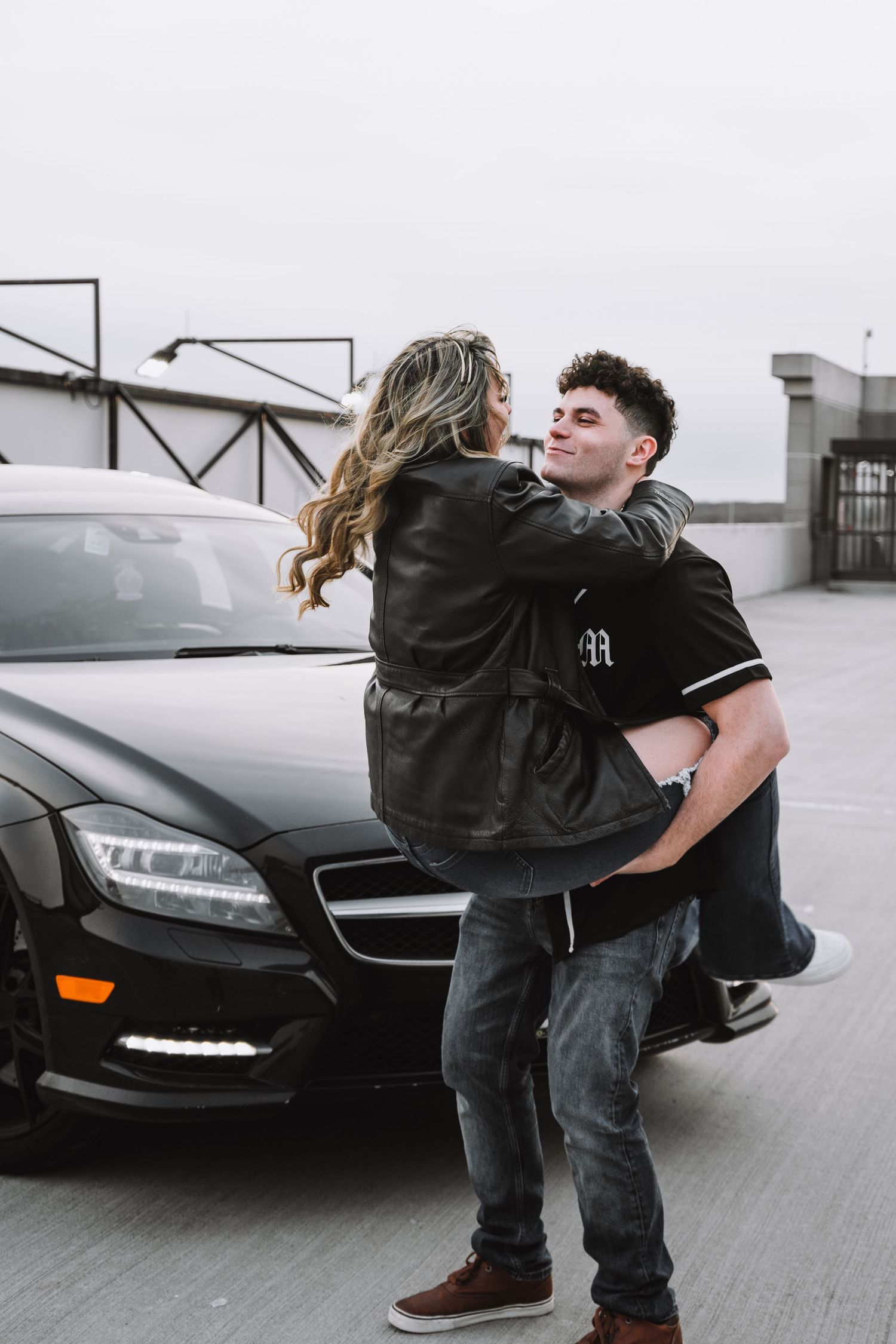 Couple sharing intimate moment against black luxury car in urban setting.