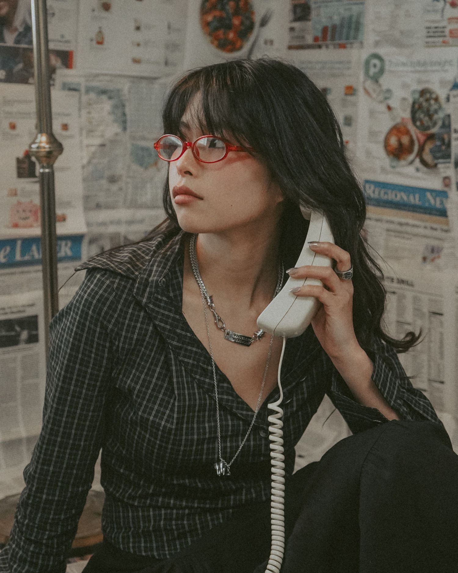 Artistic portrait in vintage setting with corded phone against newspaper-covered walls.