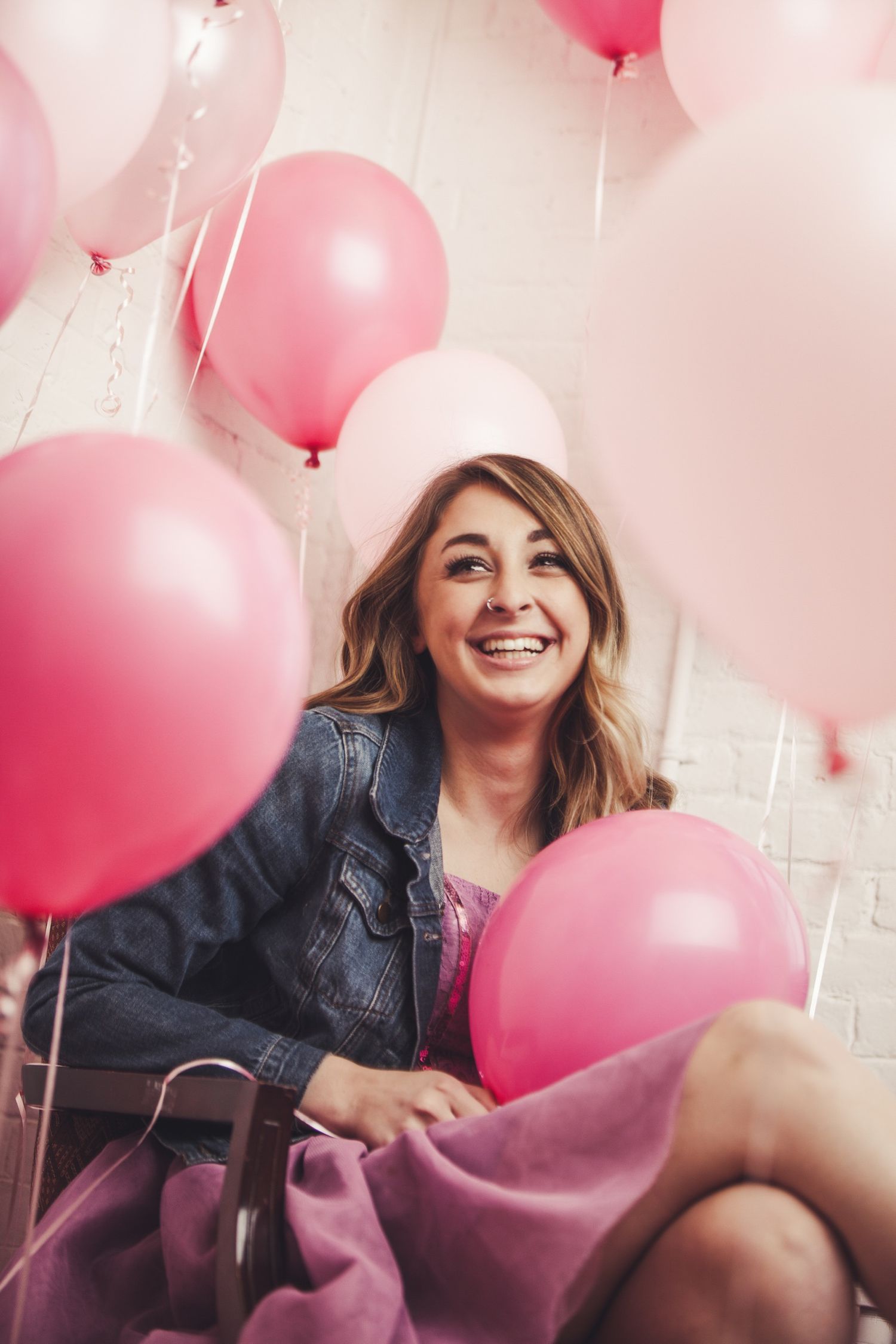 Joyful scene with pink and white balloons surrounding person in denim jacket.